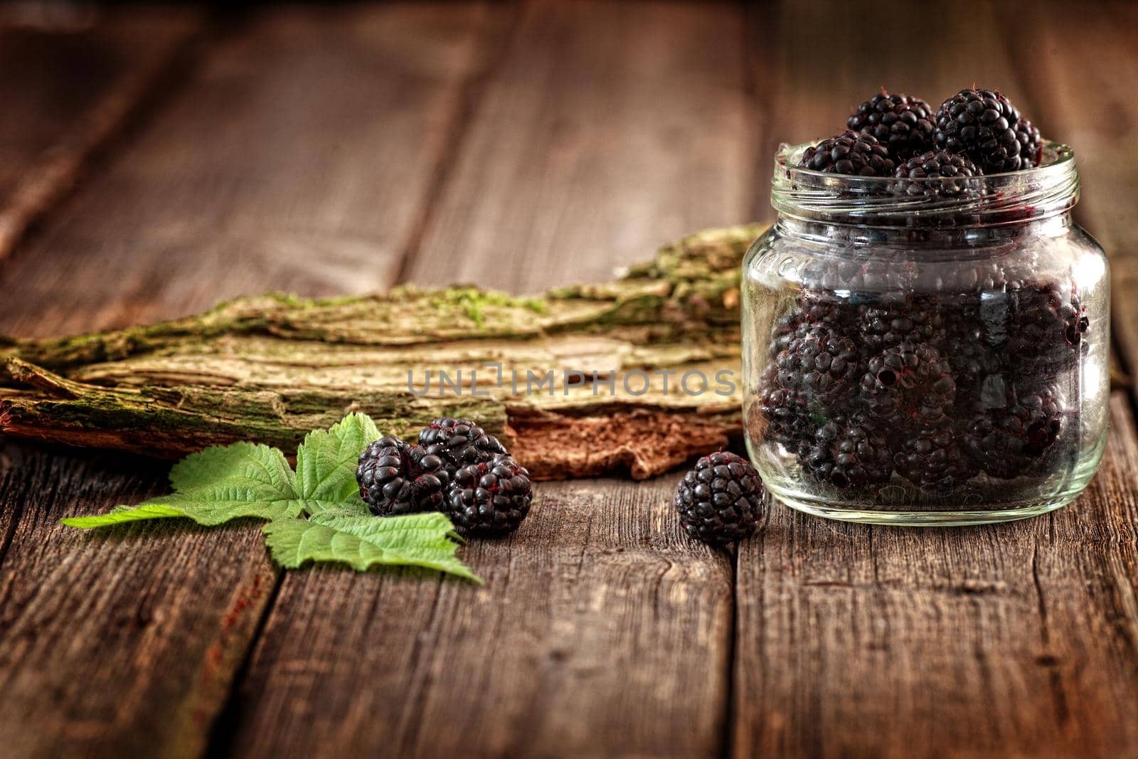 Fresh Blackberries in a glass jar on wooden table close up with