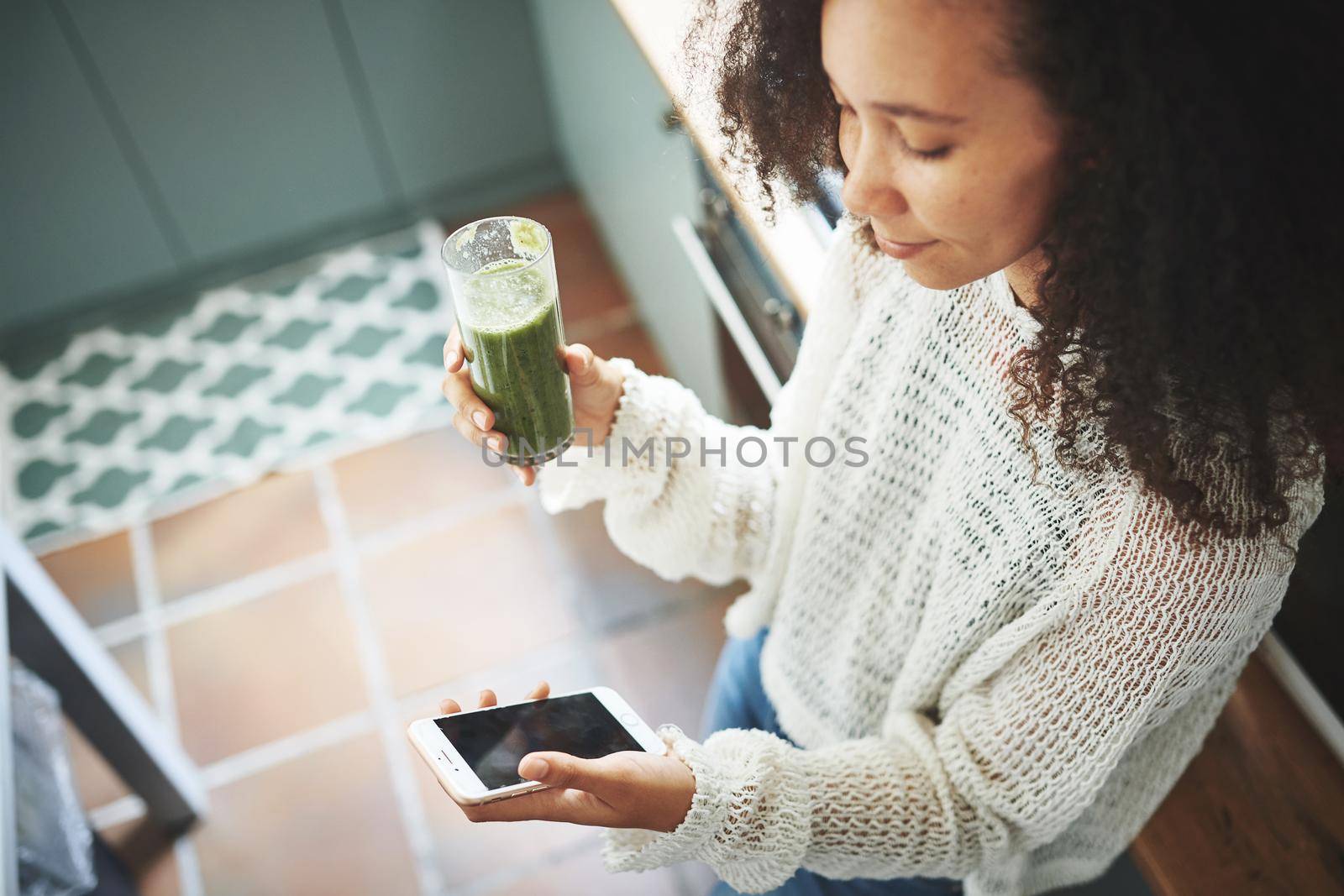 Beautiful young girl browsing on social media while enjoying her green smoothie