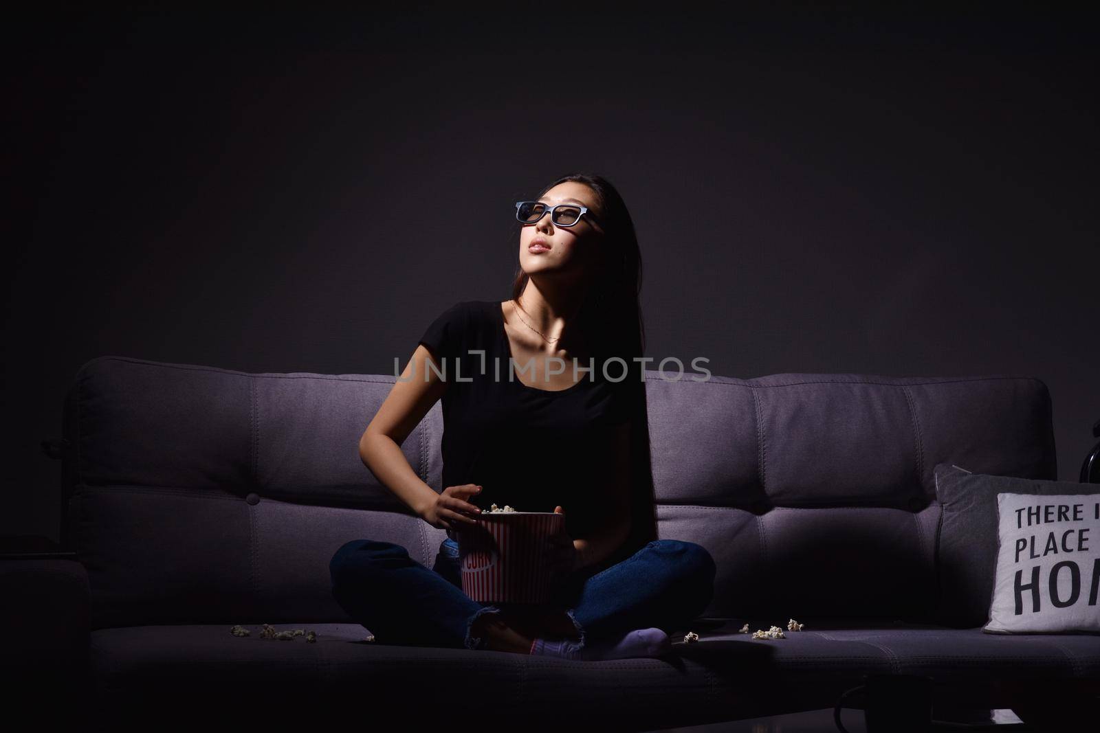 Beautiful young Asian woman watching TV at home. Eating popcorn. Time at home, isolation