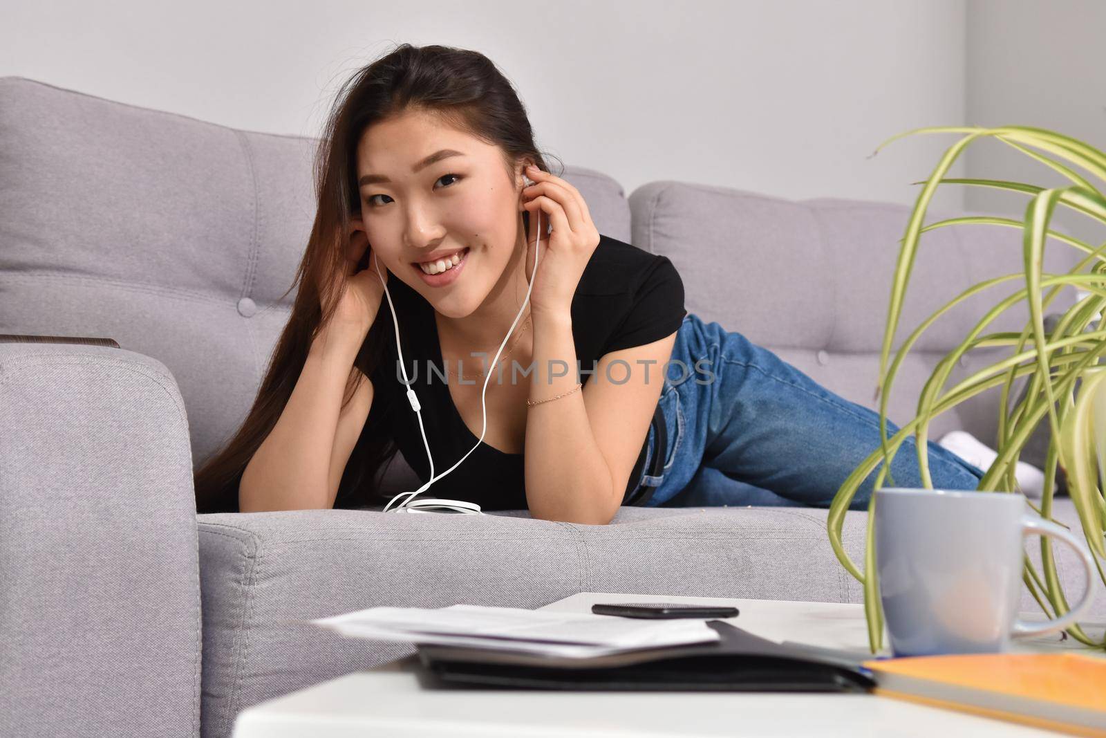 Excited beautiful asian teen listening music in headphones on her sofa at home. Wearing jeans and black tshirt