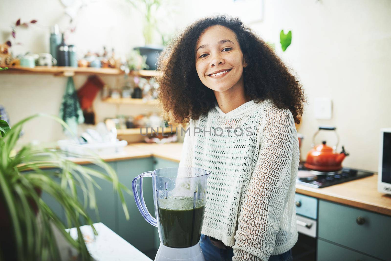 Shot of a young woman smiling at camera while making a healthy smoothie at home