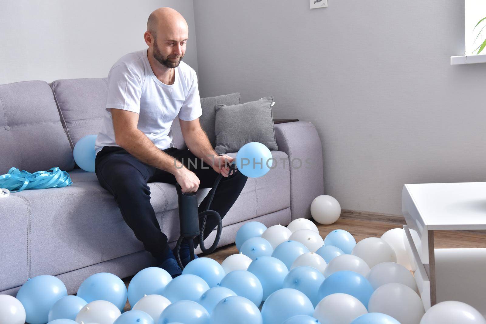 Celebration, holidays, party concept. Happy hairless man preparing to party. Blowing blue and white balloons