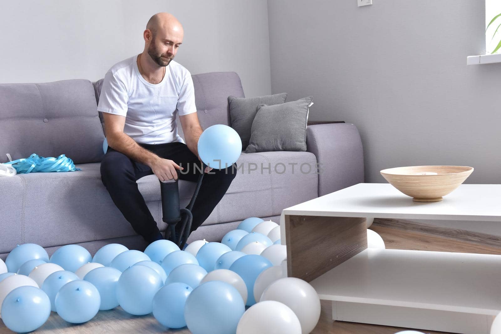 Celebration, holidays, party concept. Happy hairless man preparing to party. Blowing blue and white balloons