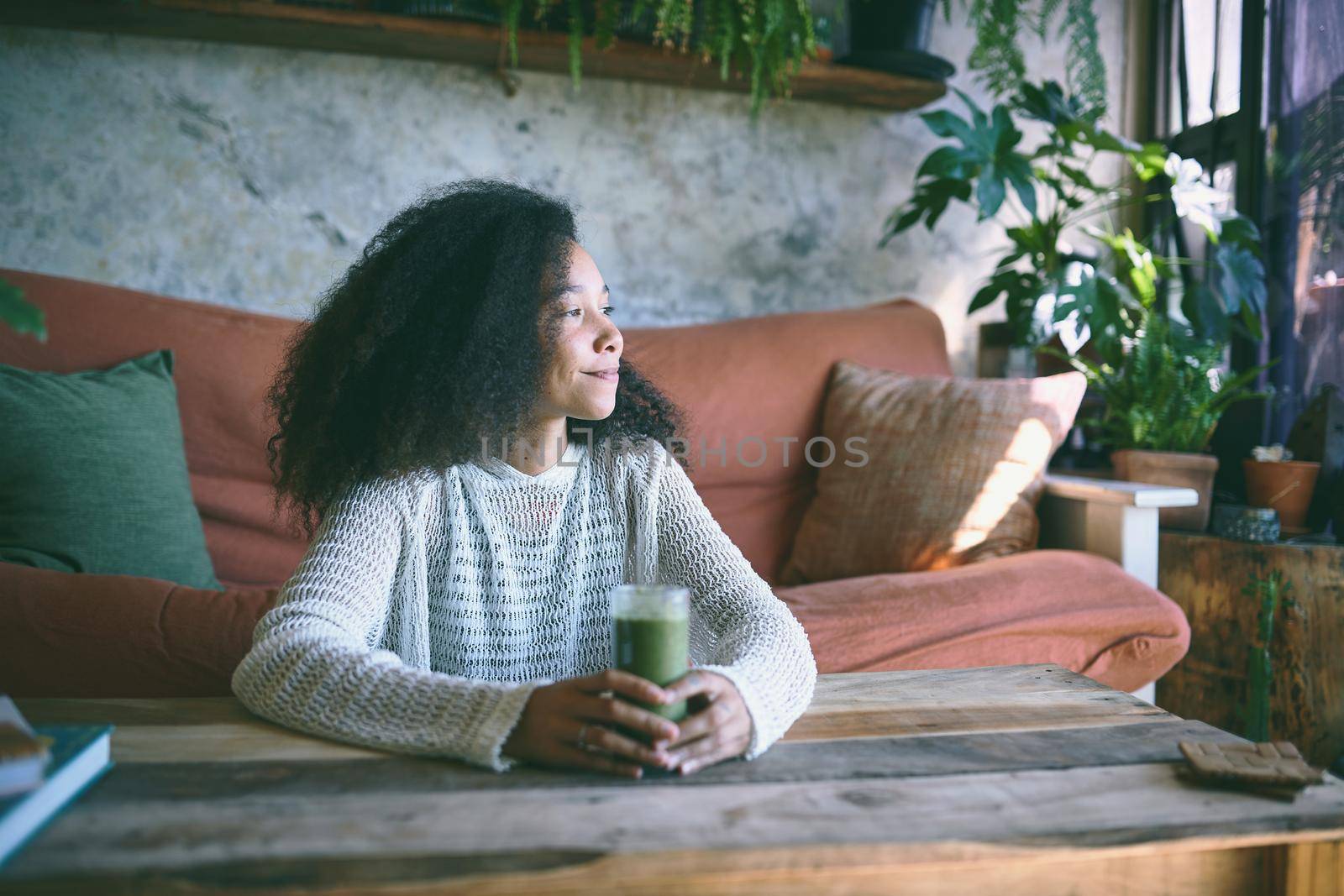 Beautiful girl sitting in her lounge staring out of the window with her smoothie in her hand