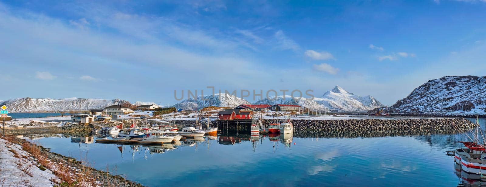 Panorama of fishing boats and yachts on pier in Norwegian fjord in village on Lofoten islands in winter, Norway