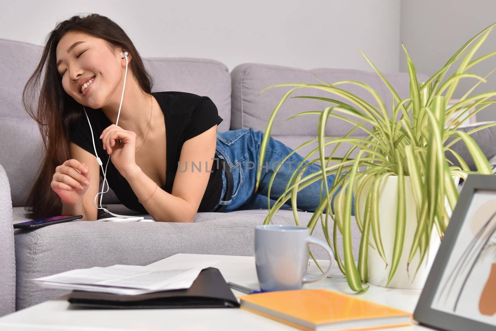 Excited beautiful asian teen listening music in headphones on her sofa at home. Wearing jeans and black tshirt