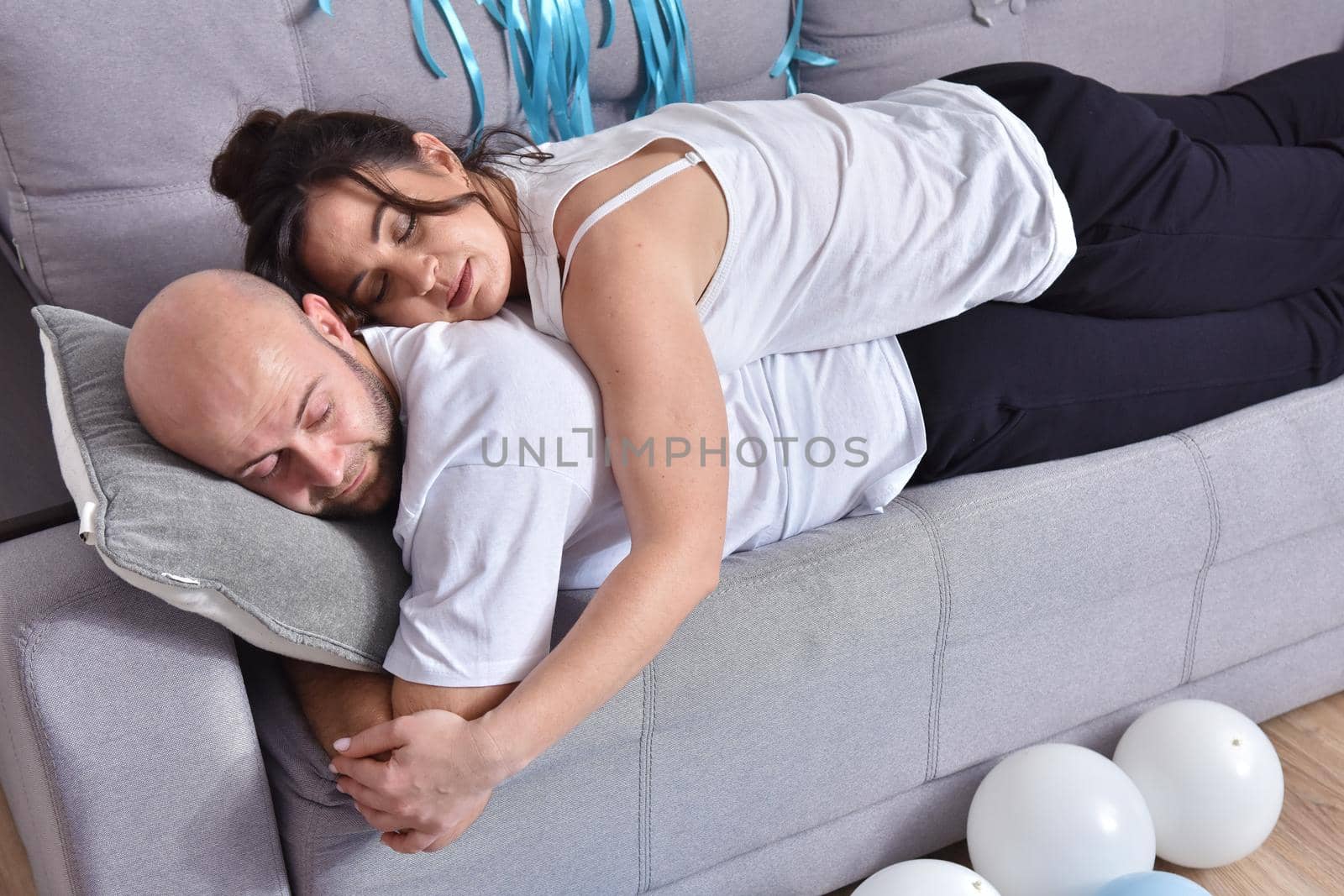 Photo of cheerful romantic caucasian family couple smiling and hugging while sitting on sofa at home. Man and woman in love