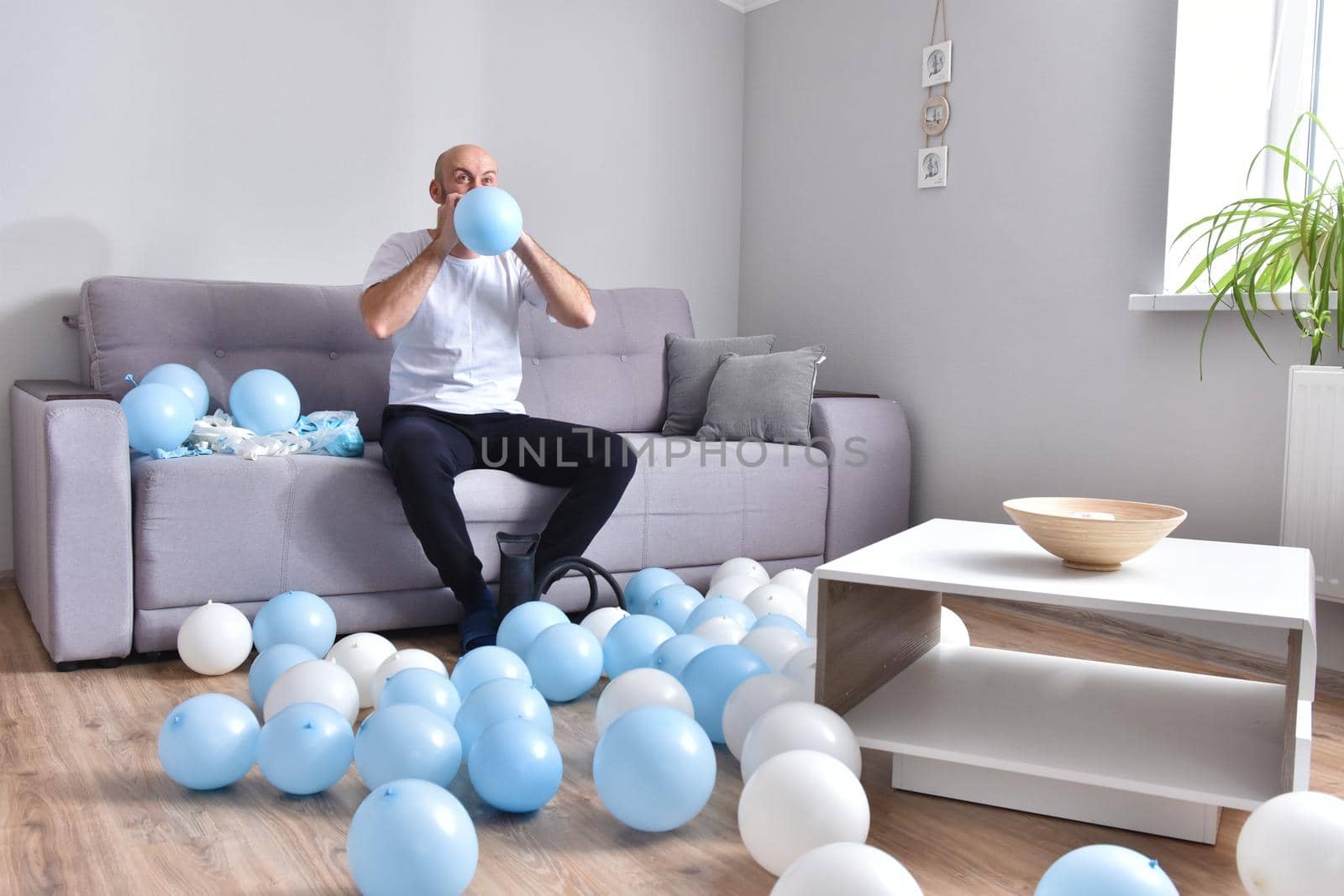 Celebration, holidays, party concept. Happy hairless man preparing to party. Blowing blue and white balloons