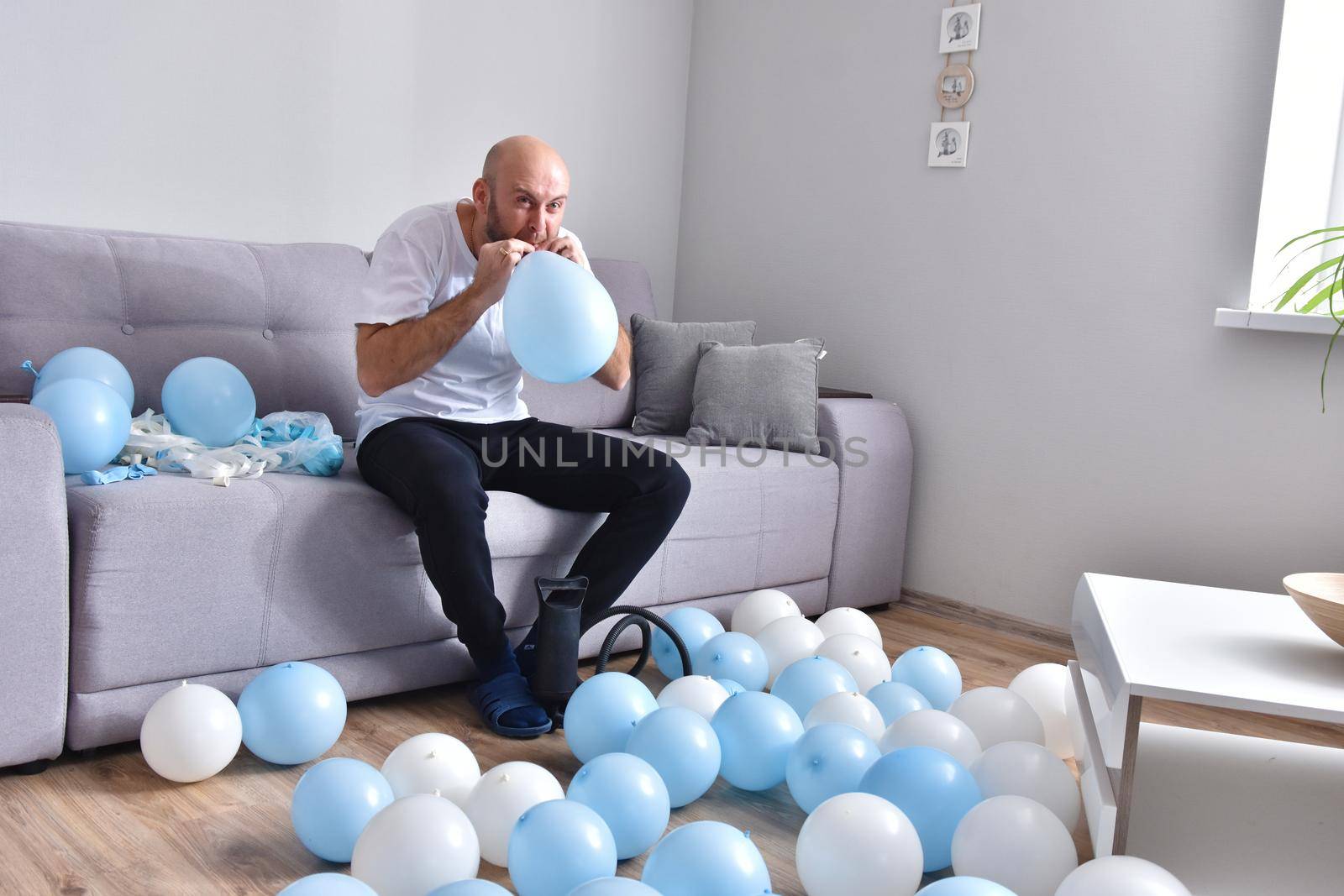 Celebration, holidays, party concept. Happy hairless man preparing to party. Blowing blue and white balloons