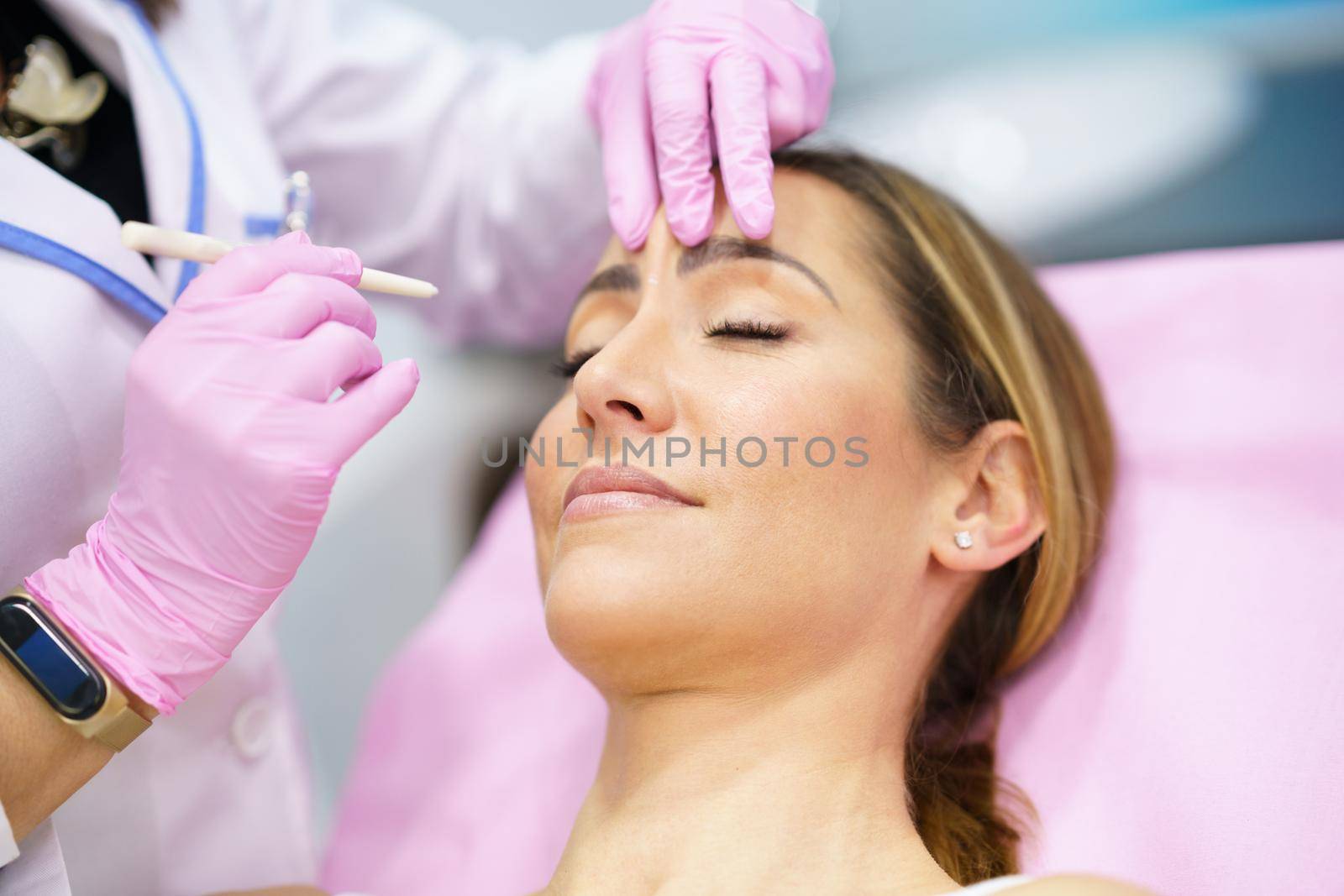 Aesthetic doctor painting on the face of his middle-aged patient the areas to be treated with botulinum toxin.