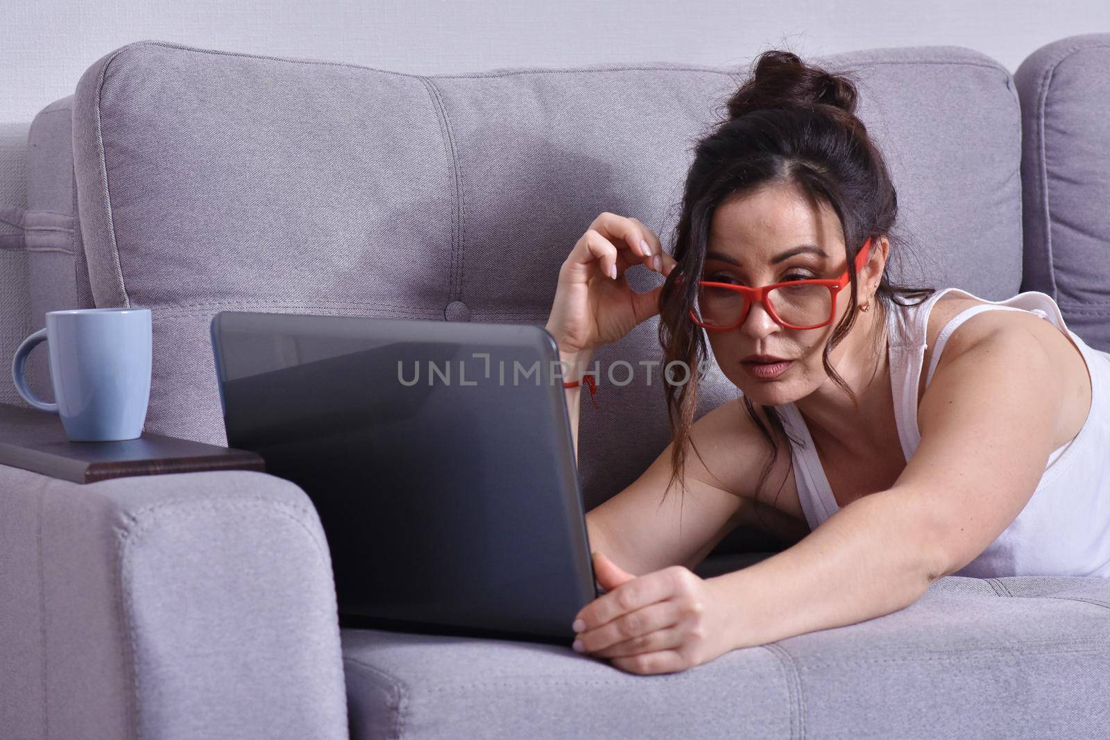 Beautiful brunette woman in red glasses on sofa using laptop