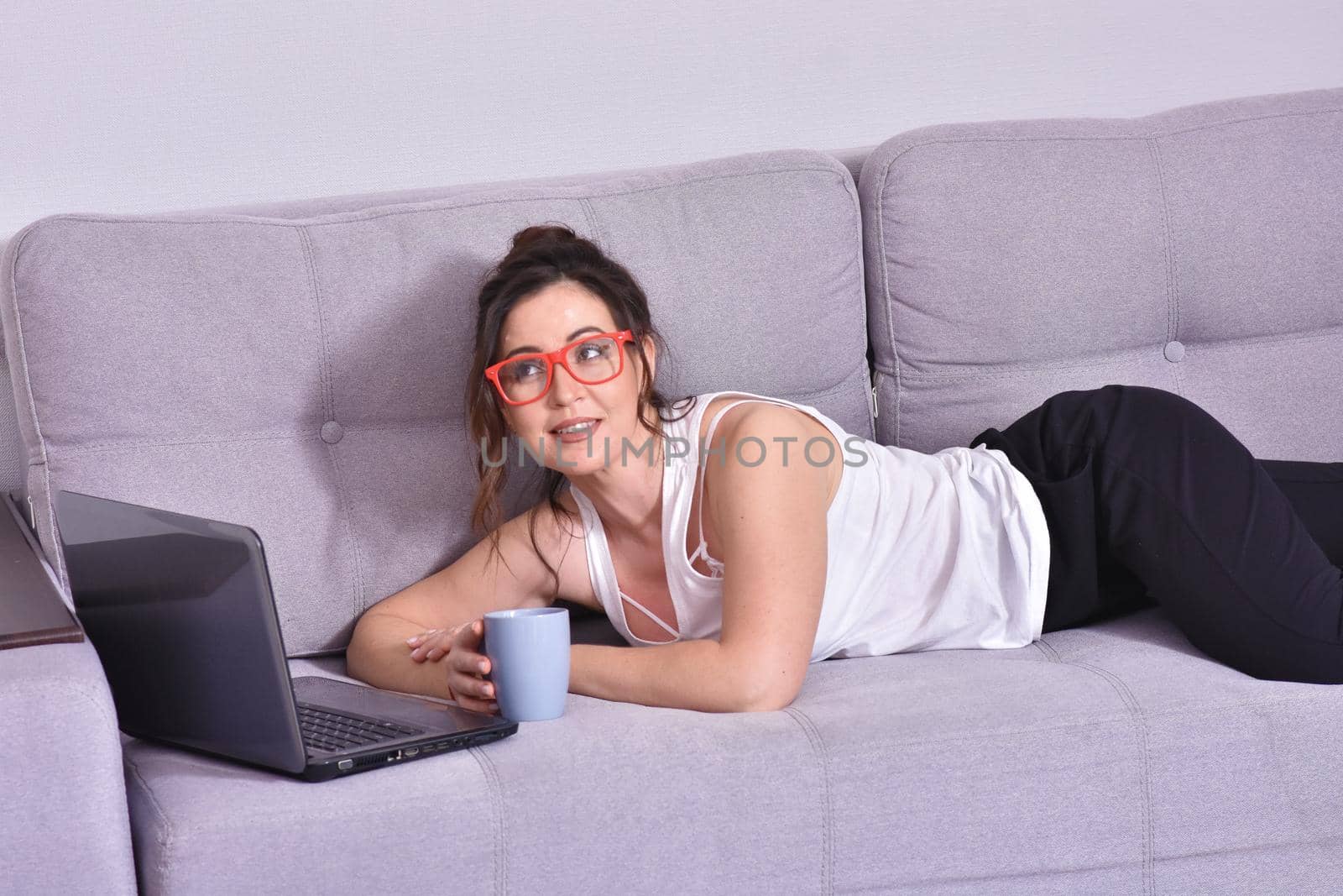 Beautiful brunette woman in red glasses on sofa using laptop