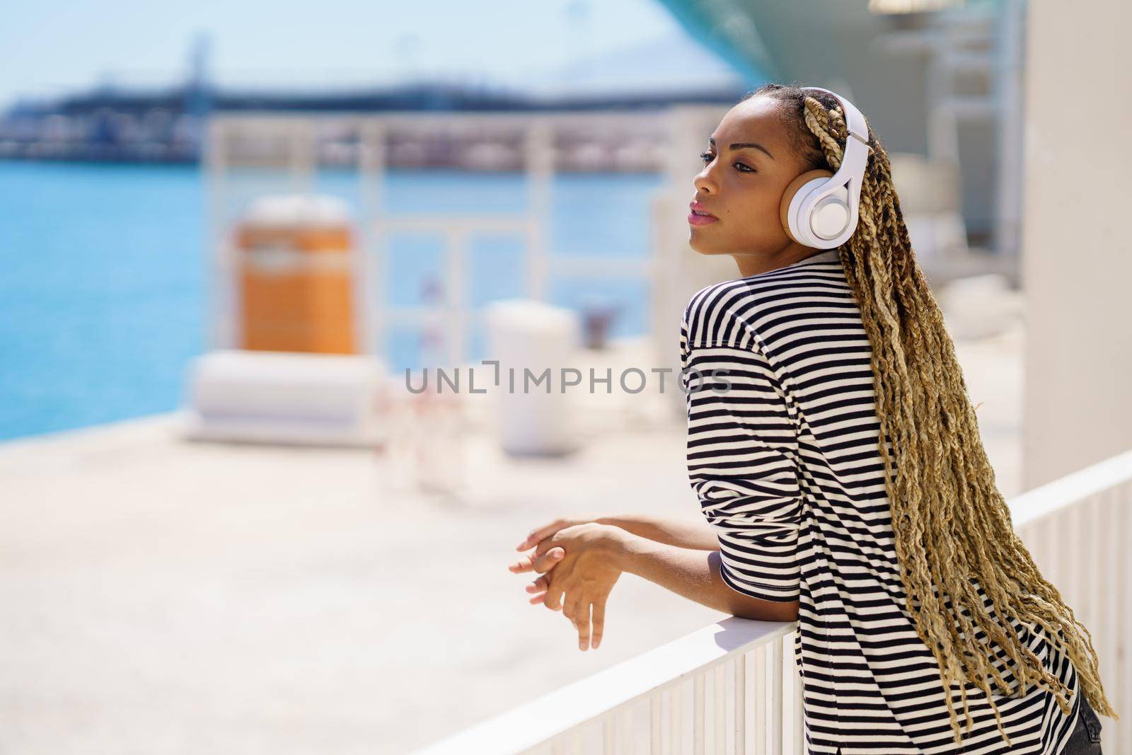 Young black woman listening to music while enjoying the view of the seaport. by javiindy