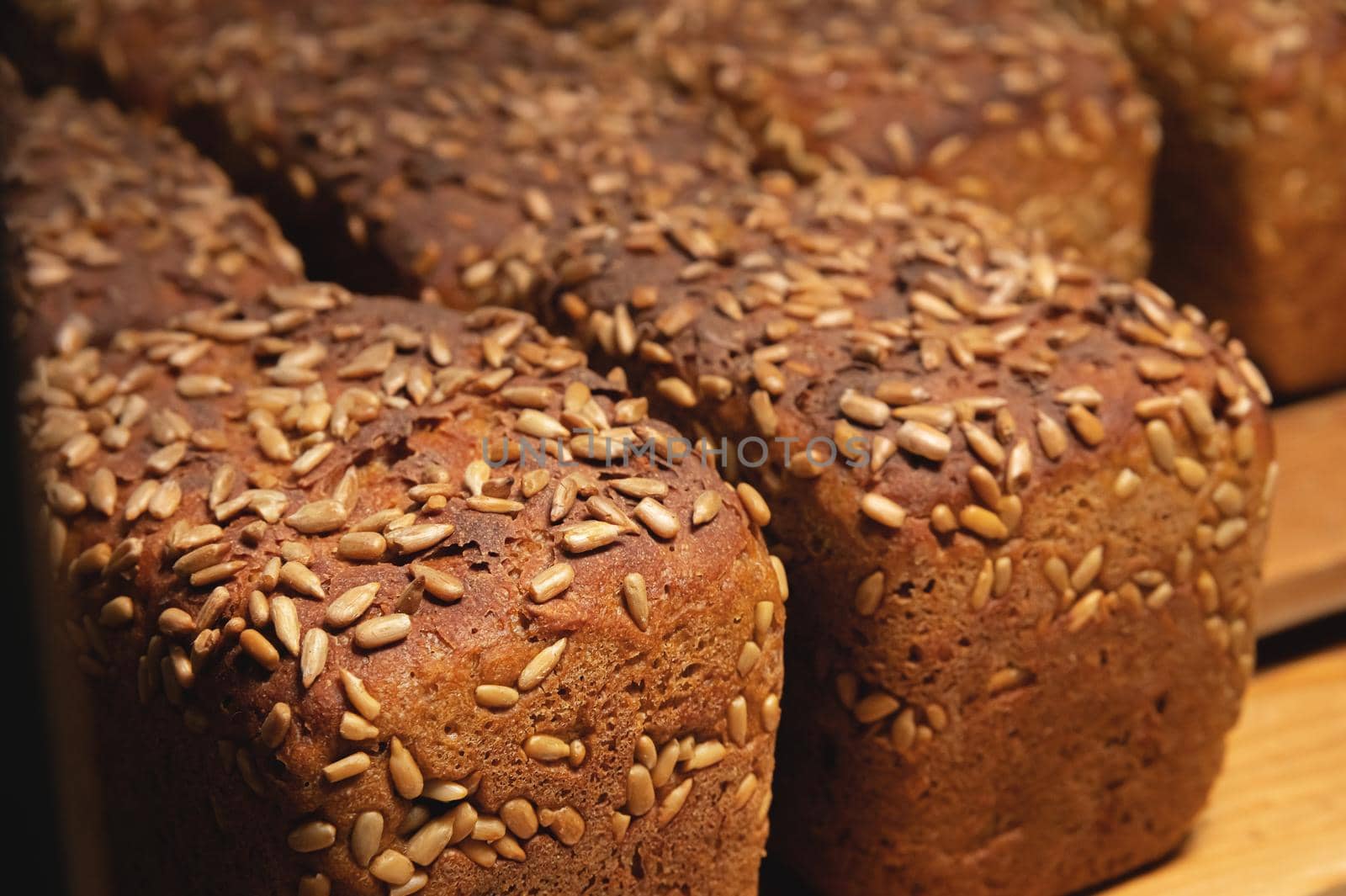 Close-up rye loaves of hot rye bread stand on a wooden tray in a dark bakery room.