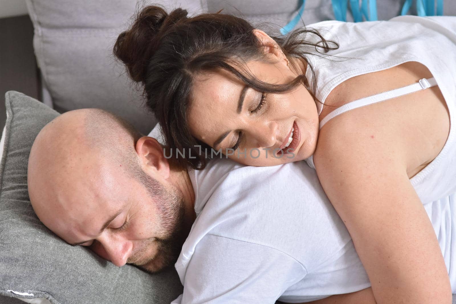 Photo of cheerful romantic caucasian family couple smiling and hugging while sitting on sofa at home. Man and woman in love