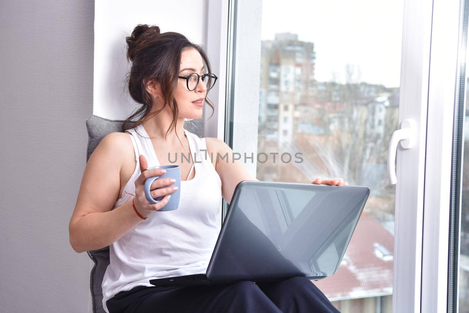 Home quarantine, protection from coronavirus. Caucasian brunette woman sit on window with computer