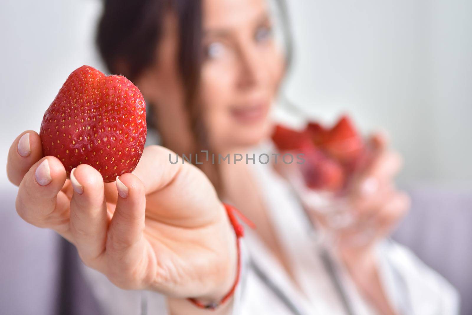 Portrait of happy young brunette woman holding bowl of juicy red strawberries