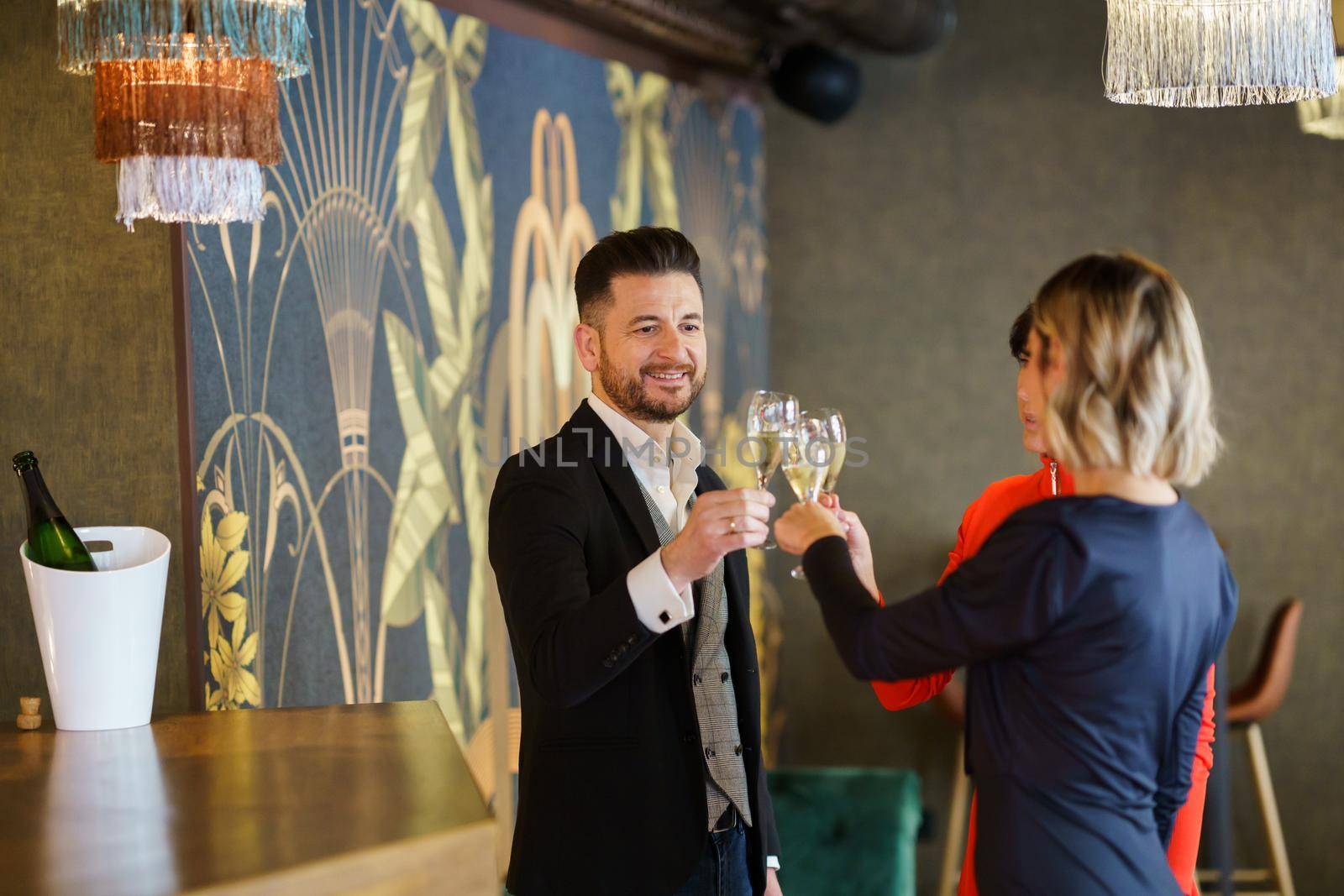 Company of cheerful friendly people in elegant outfits clicking glasses with champagne and proposing toast while celebrating event in restaurant