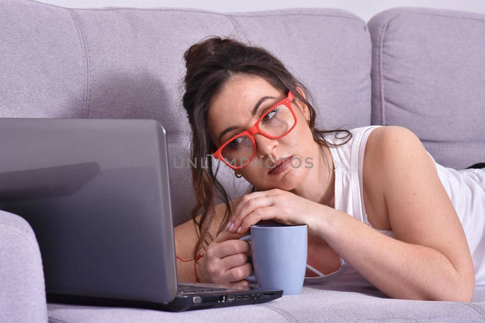 Beautiful brunette woman in red glasses on sofa using laptop