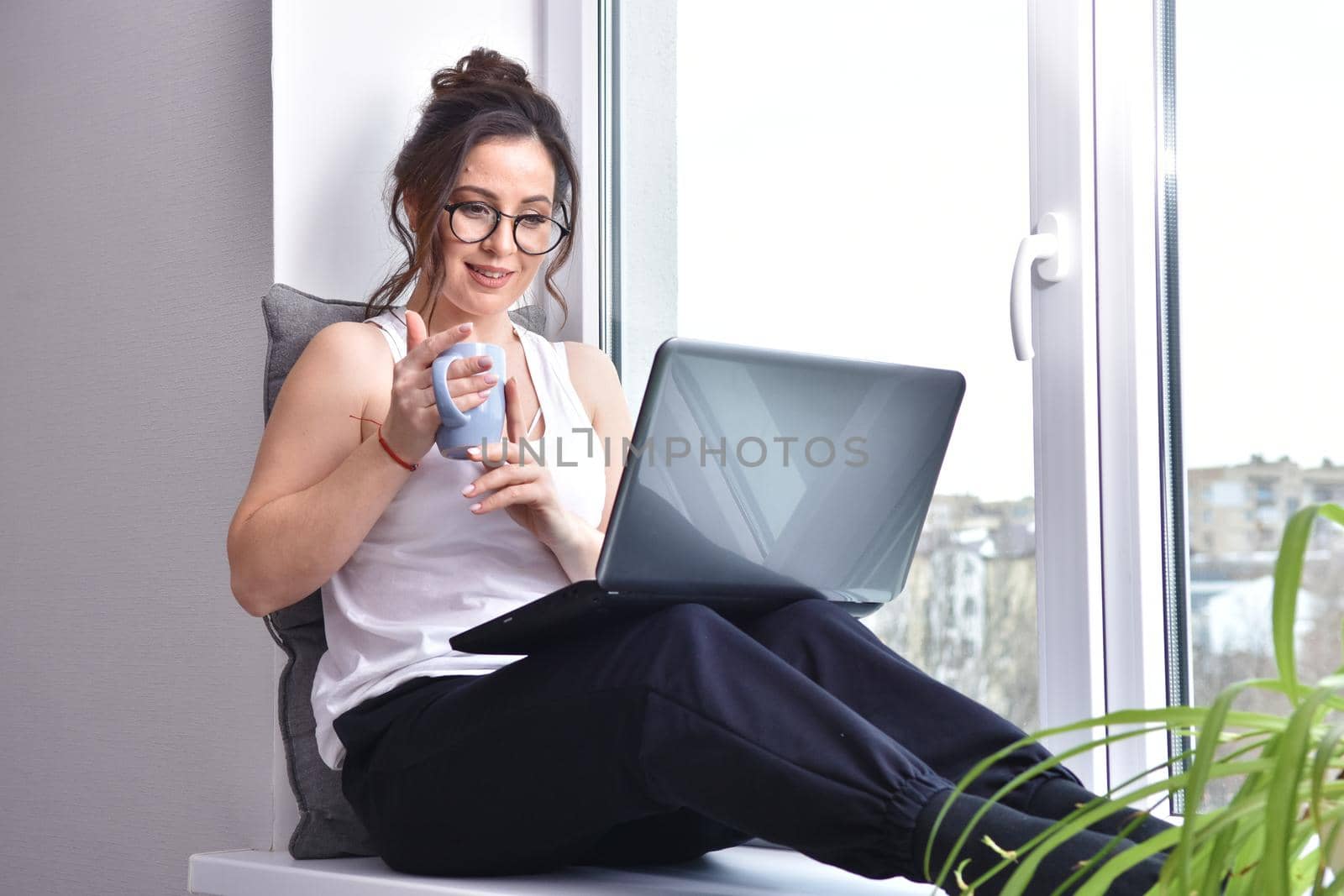 Home quarantine, protection from coronavirus. Caucasian brunette woman sit on window with computer