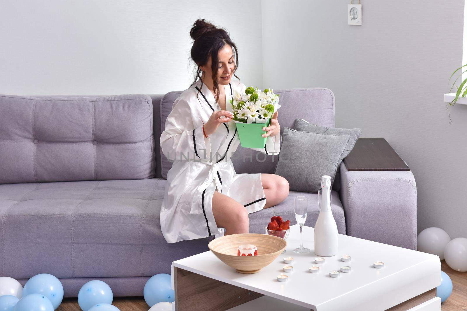 Beautiful brunette woman dressing gown with bouquet indoors. Female portrait in living room