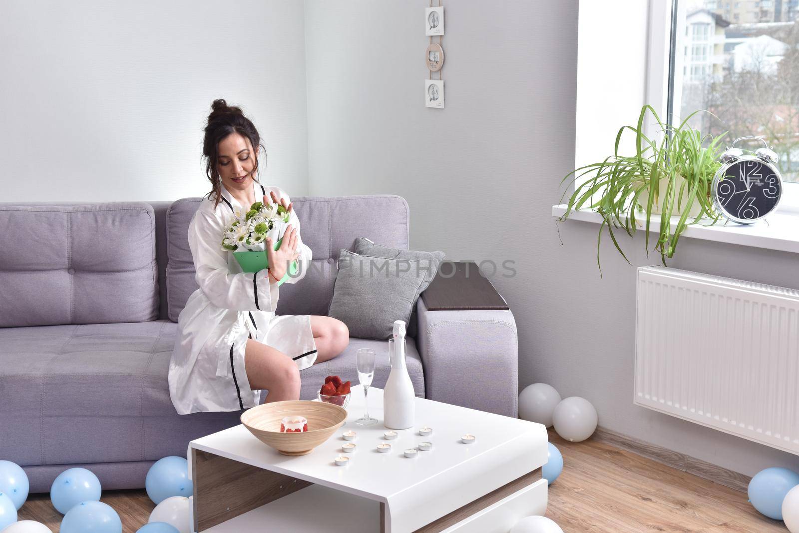 Beautiful brunette woman dressing gown with bouquet indoors. Female portrait in living room