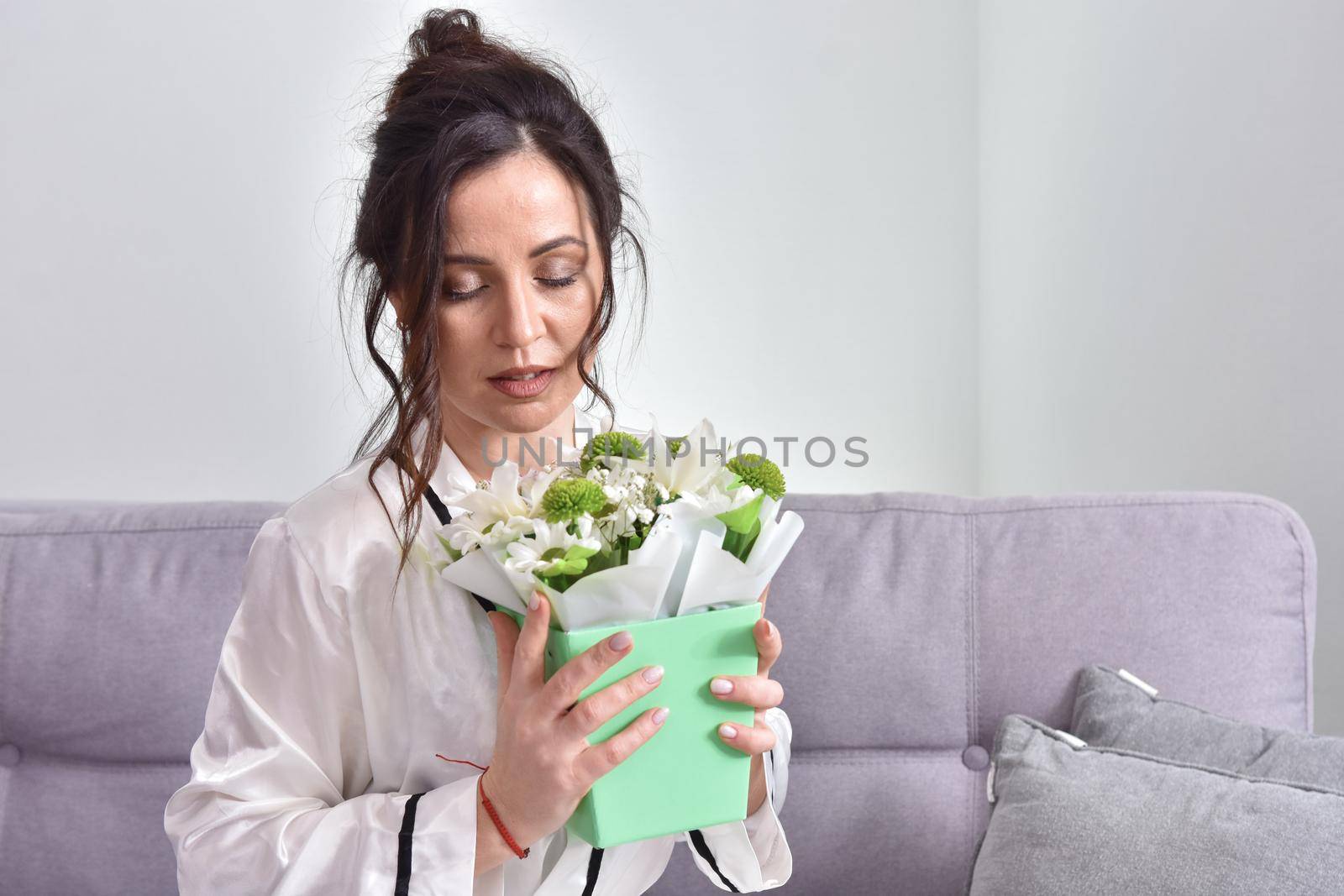 Beautiful brunette woman dressing gown with bouquet indoors. Female portrait in living room