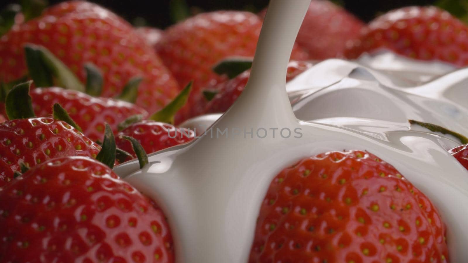 Extreme close up yogurt pouring onto strawberries on black background. Healthy fresh food concept