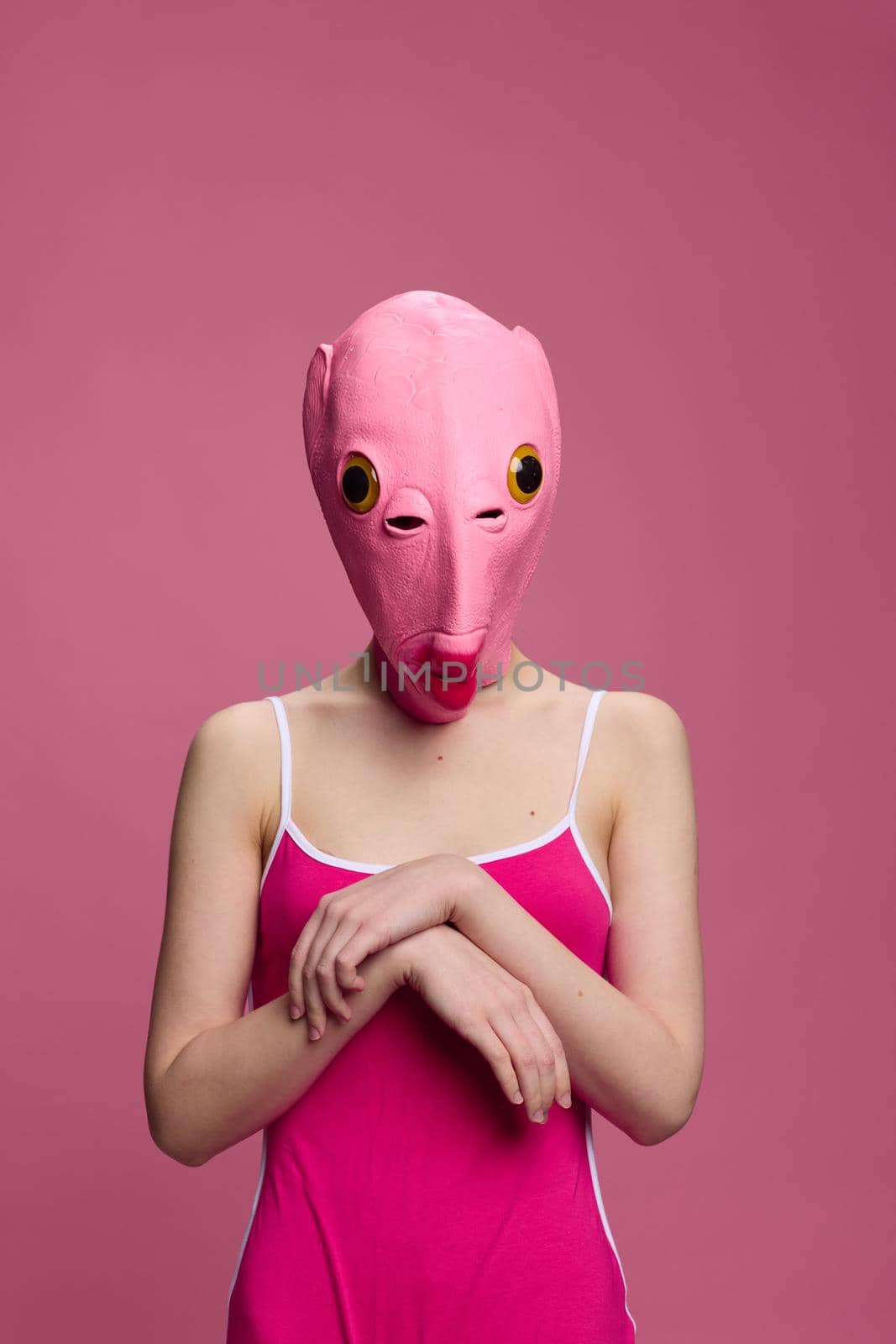 Woman standing in a pink fish mask on her head, a provocative crazy Halloween look, pink background in the studio . High quality photo