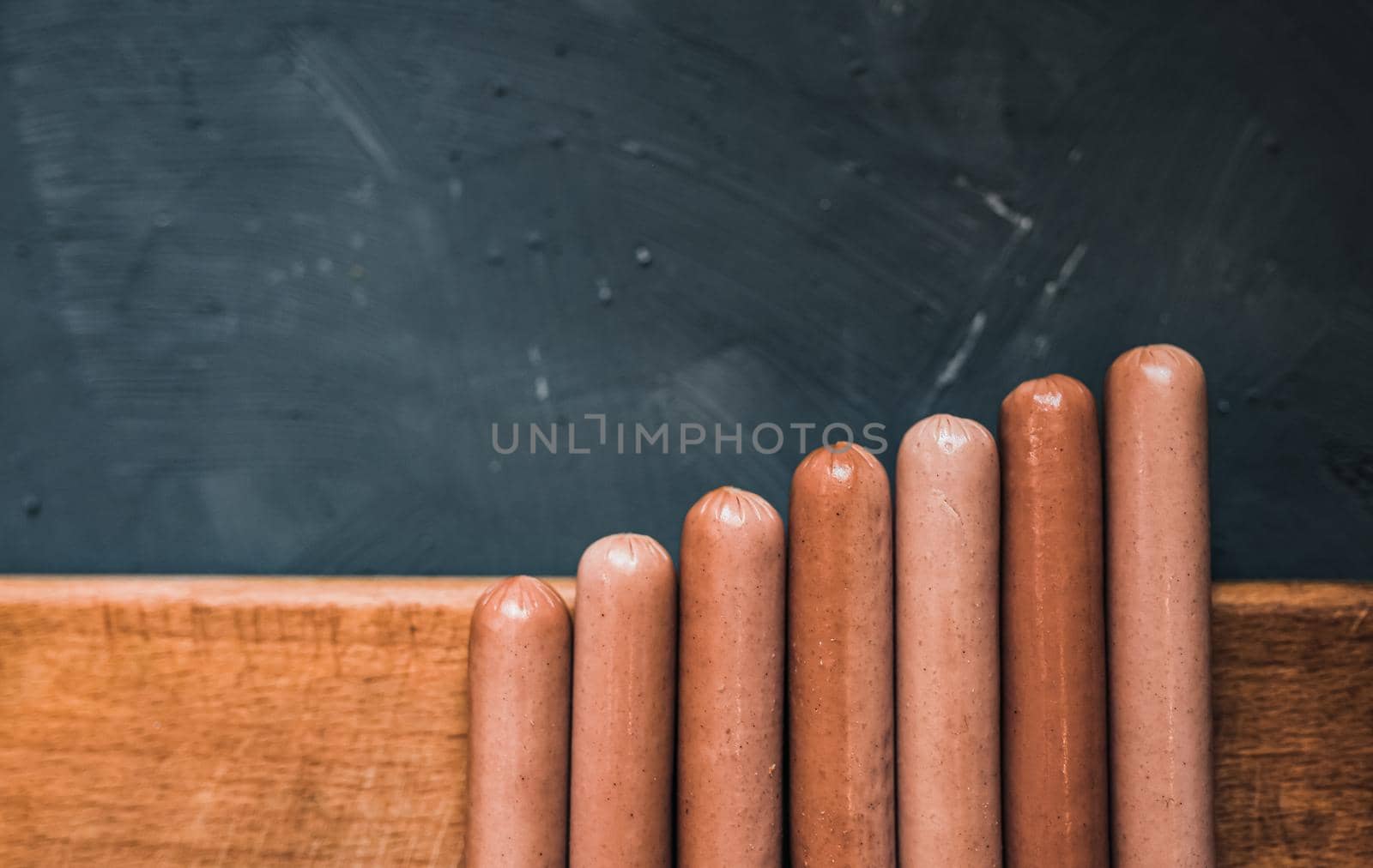 Boiled fried sausages sausages lie on a wooden kitchen board scratched against a dark concrete background.