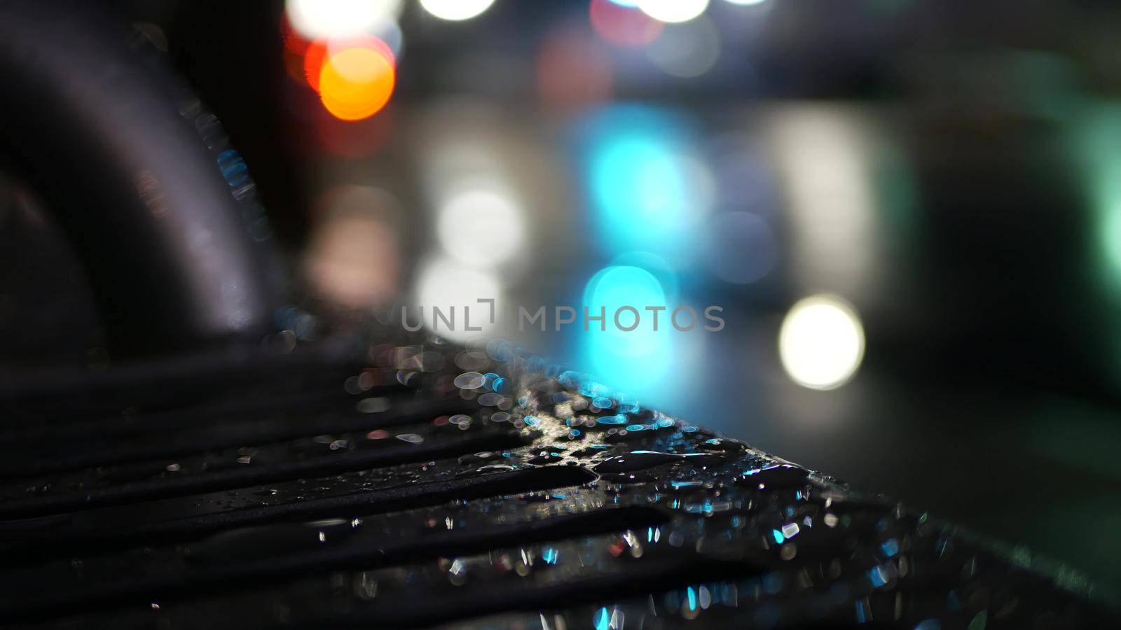 Car traffic lights reflection on bus stop bench. Water rain drops on wet metal. by DogoraSun