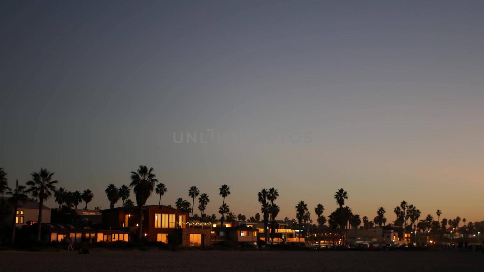 Palm trees silhouettes in twilight sky, California beach, USA. Beachfront houses by DogoraSun