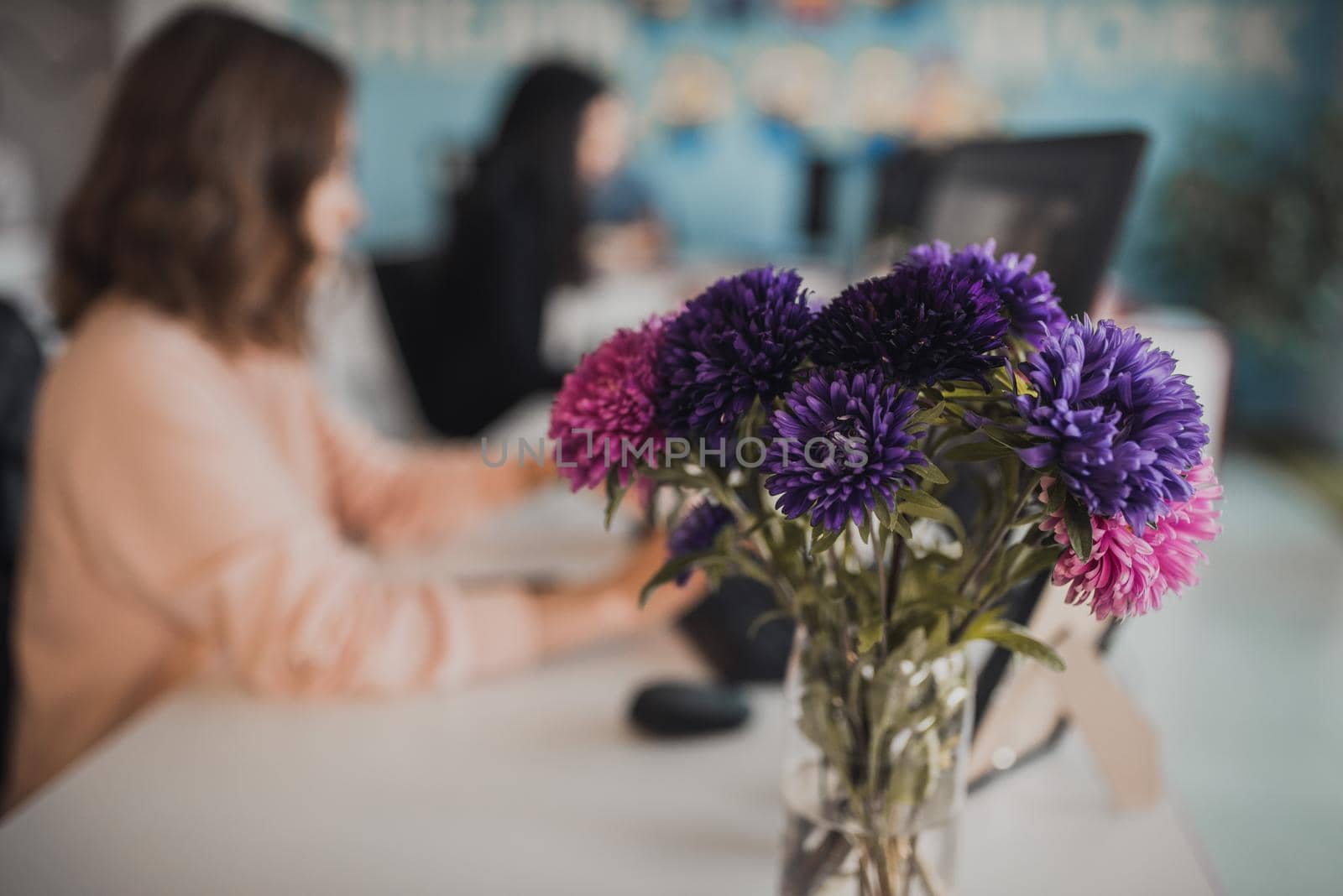 A bouquet of multi-colored pink and purple flowers on the background of a woman working at the computer.