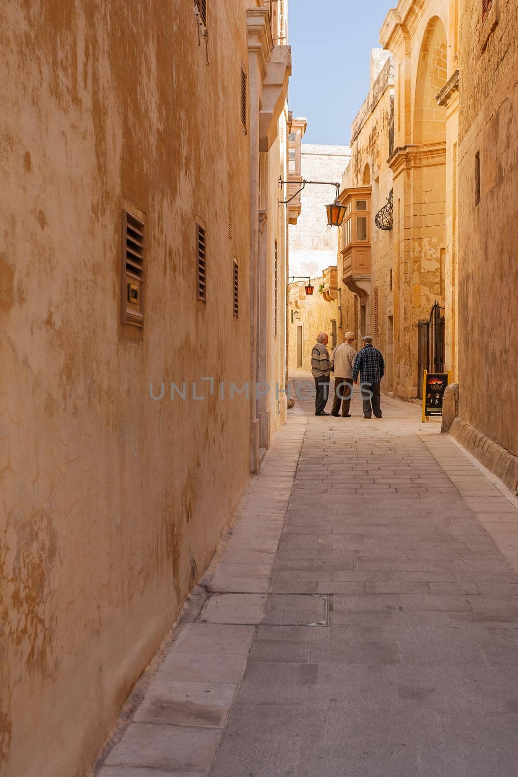 MDINA, MALTA - February 18, 2010. Local old men on narrow street of Mdina, old capital of Malta. Stone buildings with old fashioned doors and balconies. by aksenovko