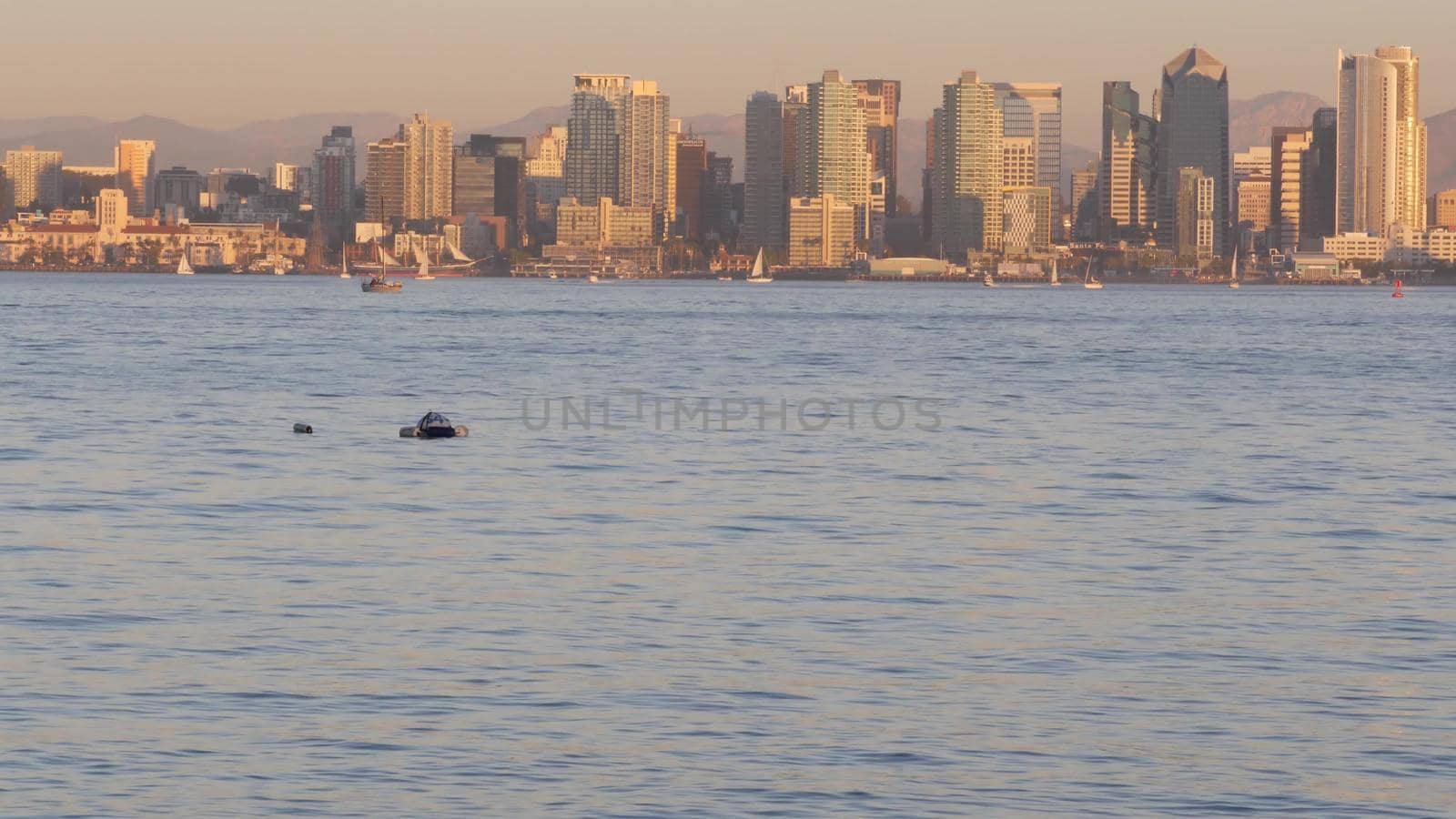 Downtown city skyline at sunset, San Diego cityscape, California coast USA. Highrise skyscrapers by bay, waterfront promenade. Urban architecture by harbor. Seamless looped cinemagraph. Shelter island