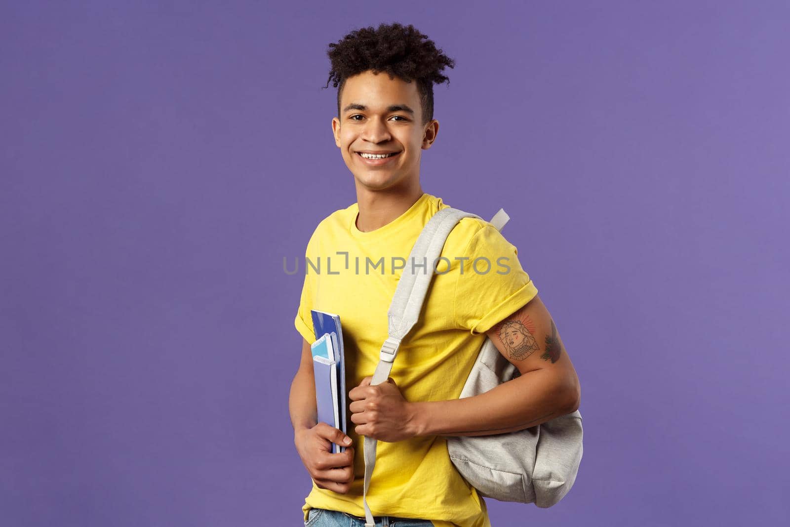 Back to school, university concept. Portrait of handsome charismatic hispanic guy, student walking to campus, going for lecture, studying hold backpack and notebooks, stand purple background.