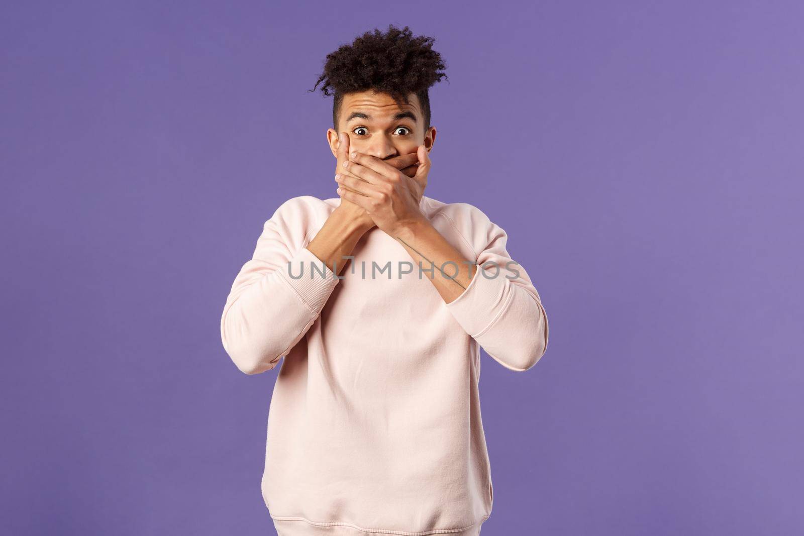 Portrait of shocked impressed young hispanic man found out gossip, heard rumour, trying not laugh shut his mouth with hands and express amazement and surprised with gaze, purple background by Benzoix