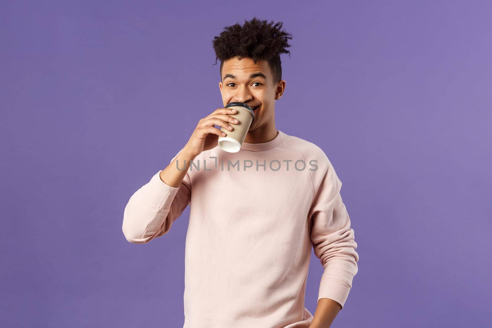 Leisure, lifestyle and people concept. Portrait of young cheerful guy drinking coffee take-away from favorite cafe, smiling enjoying nice spring day, standing purple background.