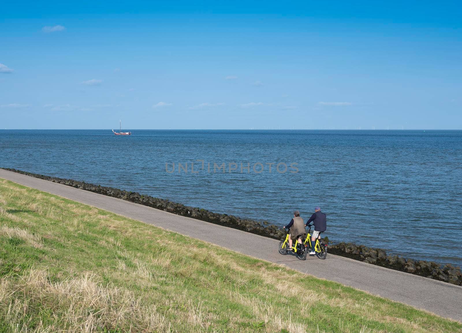 couple rides bicycle on dike of wadden sea on dutch island of texel in summer by ahavelaar