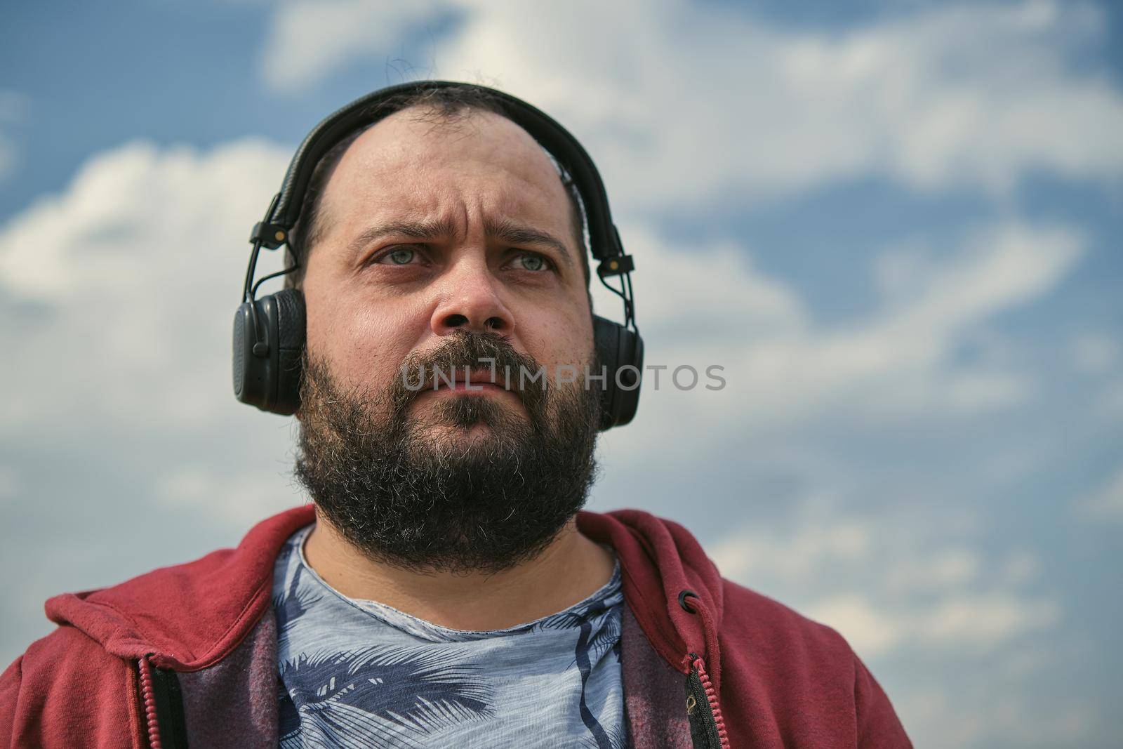 Middle-aged European man in headphones outdoors listening to music against the background of the sky