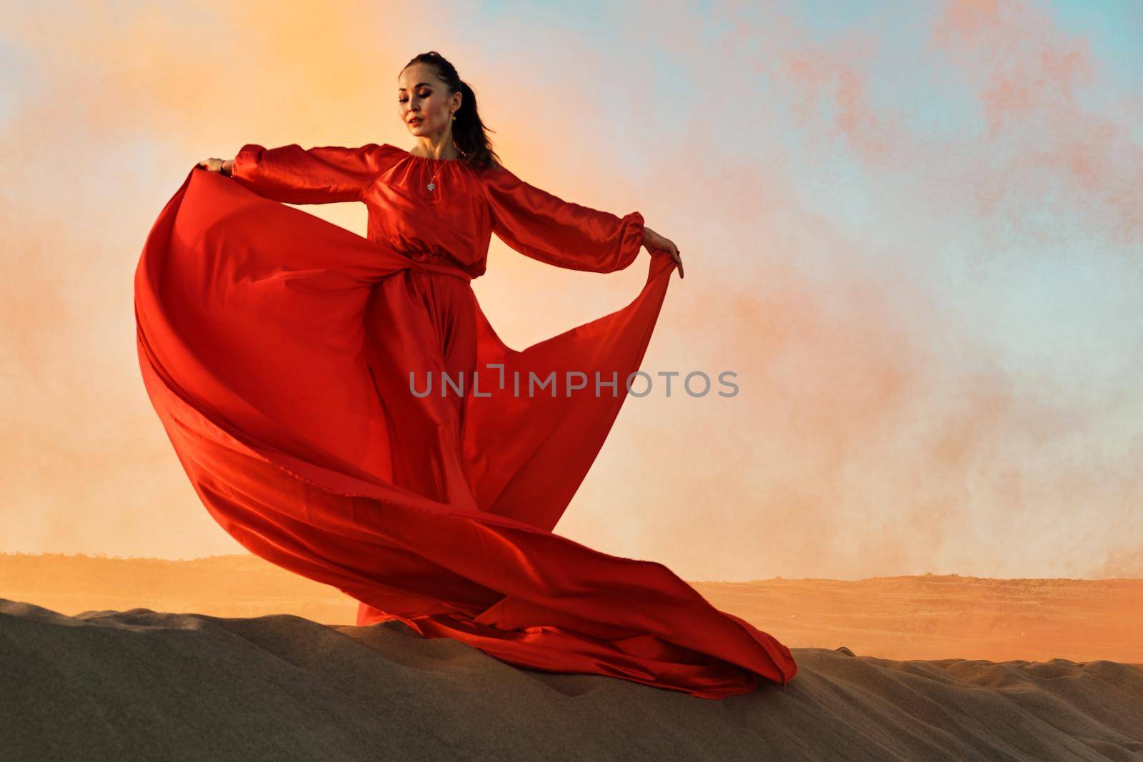 Woman in red dress dancing in the desert at blue sky