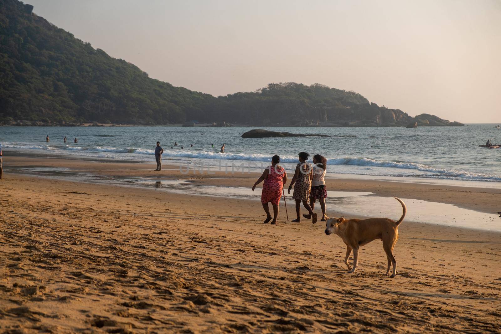 A family, mother and two daughters walking together on a beach in Goa at sunset