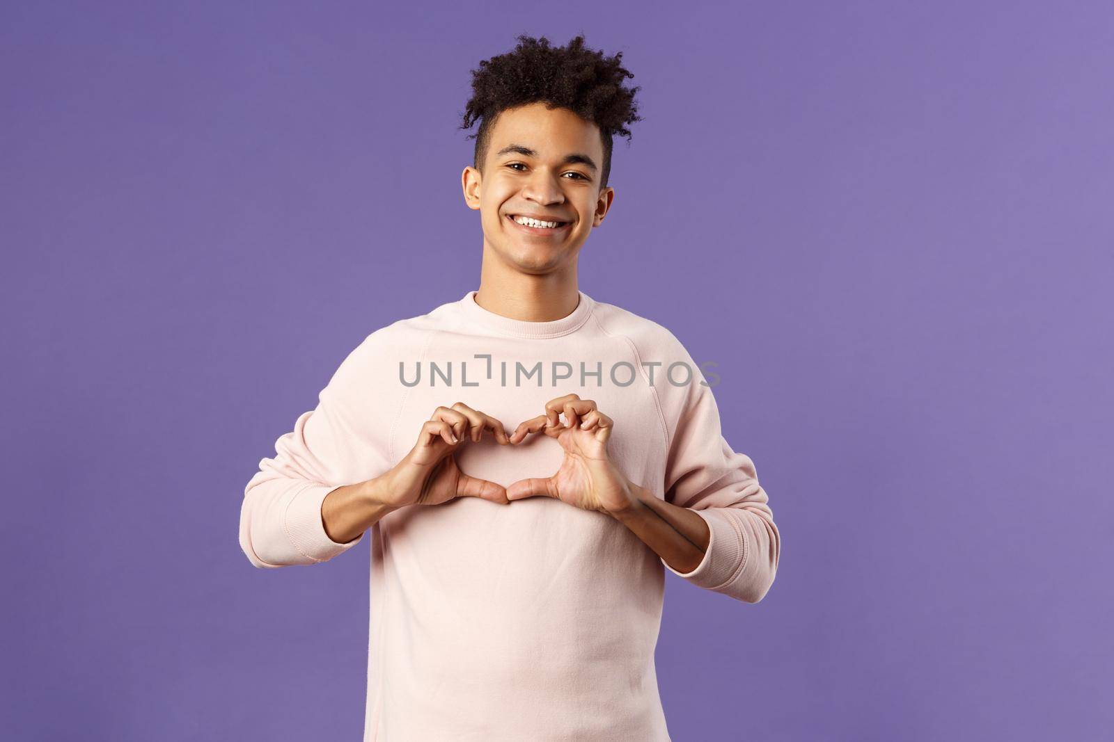 Portrait of young happy, romantic lovely boyfriend express his love and sympathy to dearest person, show heart sign and beaming smile, like this girl and trying to confess feelings, purple background by Benzoix