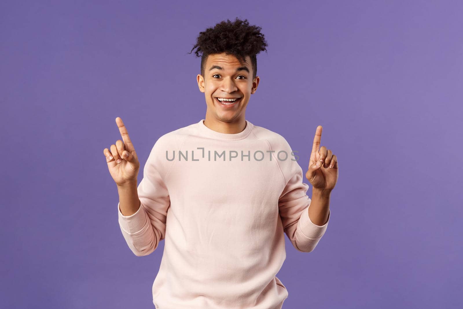Portrait of charismatic lively young man heard about good deal, asking question intrigued, pointing fingers up, smiling upbeat at camera, look with interest, recommend product, purple background.