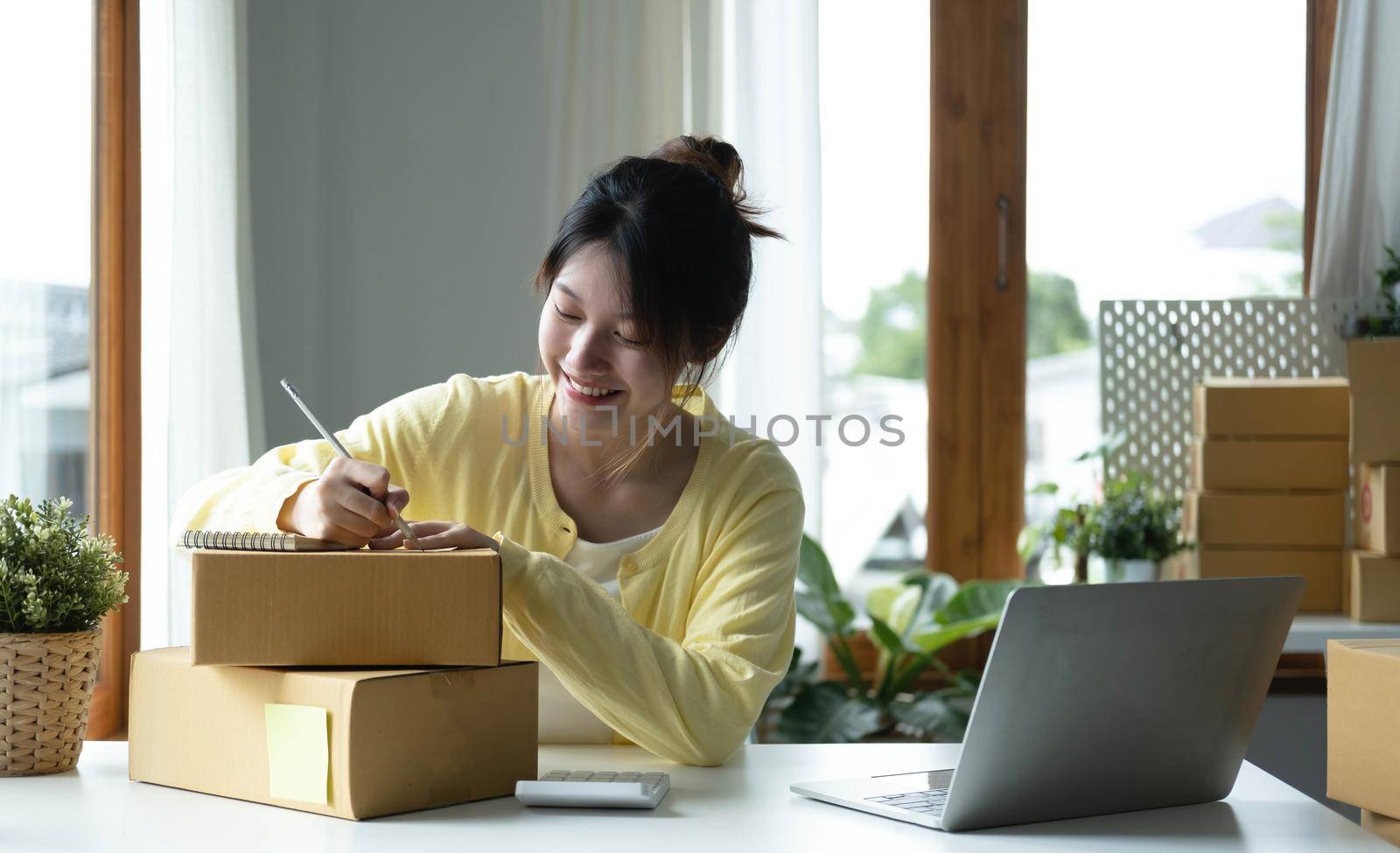 Starting small businesses SME owners female entrepreneurs Use a laptop or notebook to receive and review orders online to prepare to pack boxes, sell to customers, SME online business ideas. by wichayada