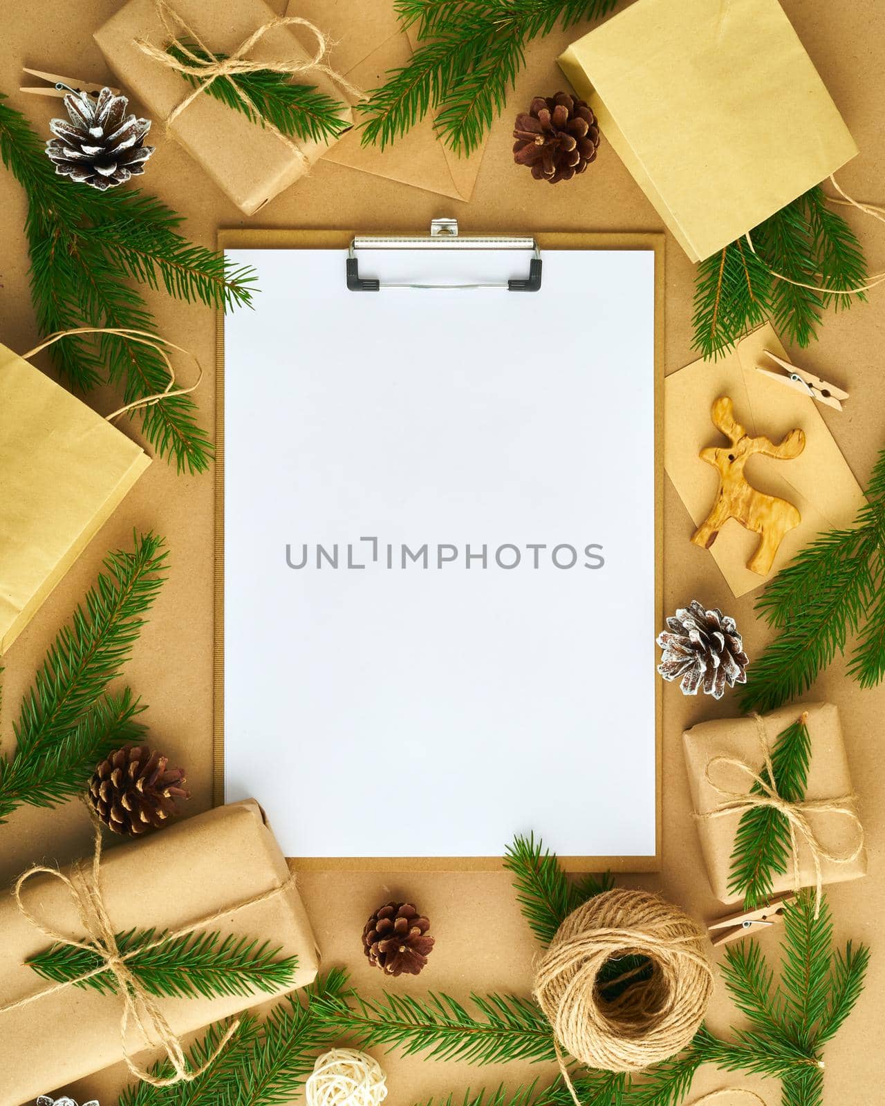 White open blank on clipboard and Christmas decoration lying on beige craft paper background, flat lay, copyspace. Hand crafted, plastic free, zero waste concept, vertical