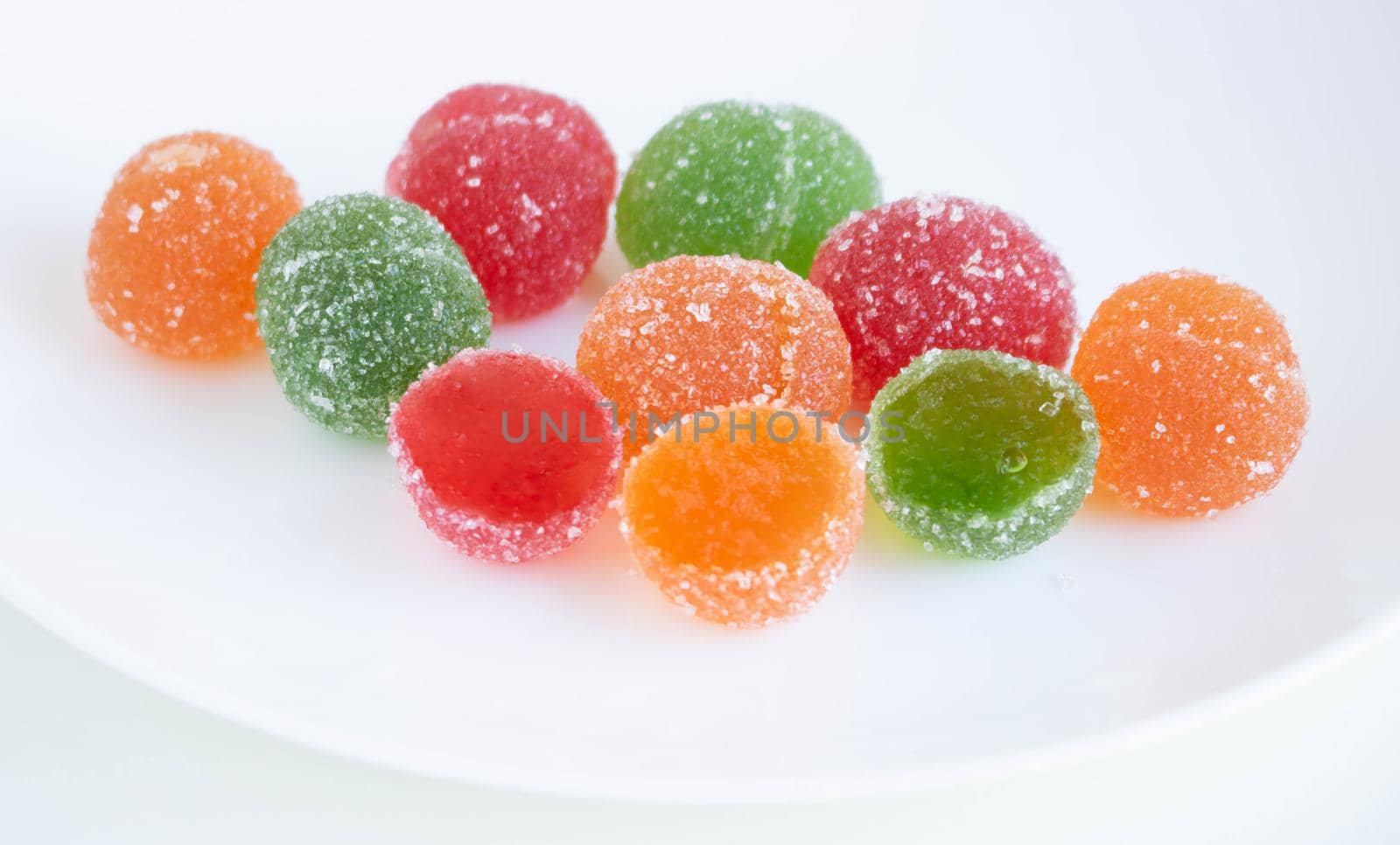 A pile of red, green and yellow jelly cubes on a white plate on a white background by lapushka62