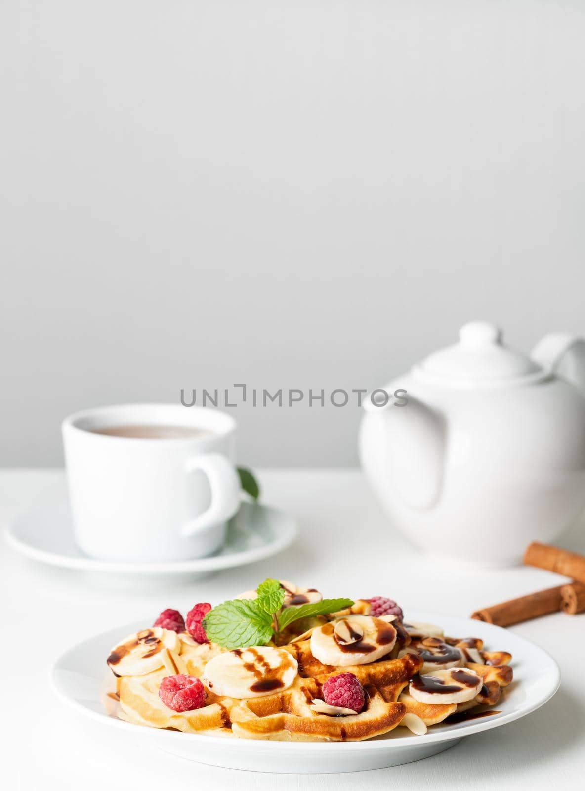 Belgian curd waffles with raspberries, banana, chocolate syrup. Breakfast with tea on white background, side view, vertical by NataBene