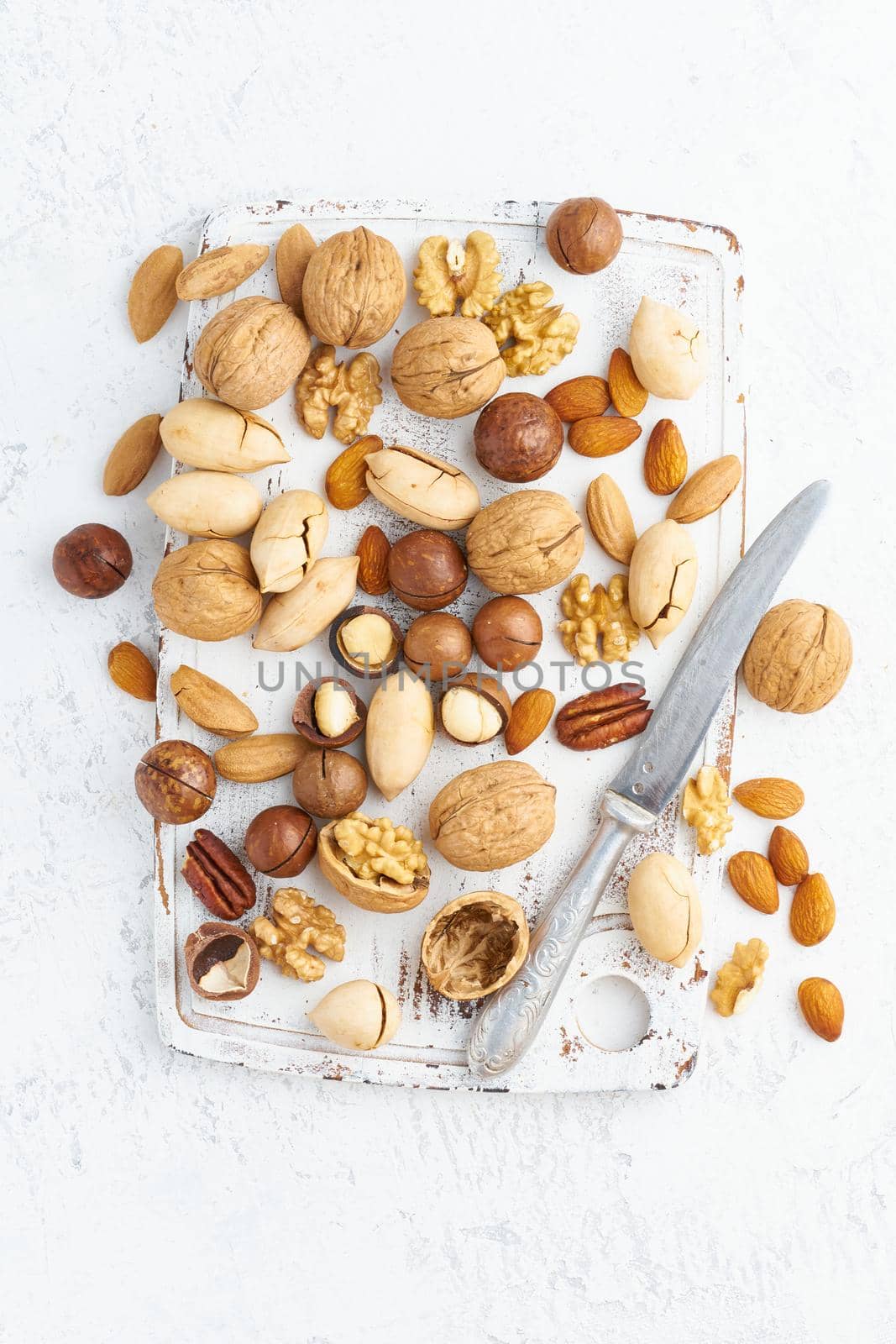 Mix of nuts - walnut, almonds, pecans, macadamia and knife for opening shell on a white wooden cutting board. Healthy vegan food. Clean eating, balanced diet. Top view, macro, close up