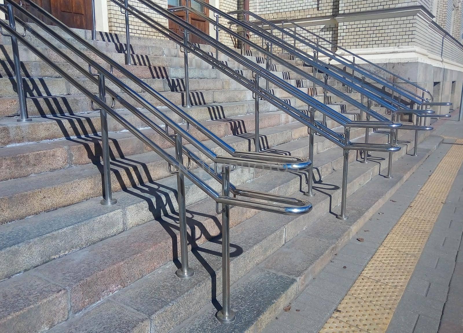 Railing shadows on steps of modern granite staircase. Light and shadow pattern.
